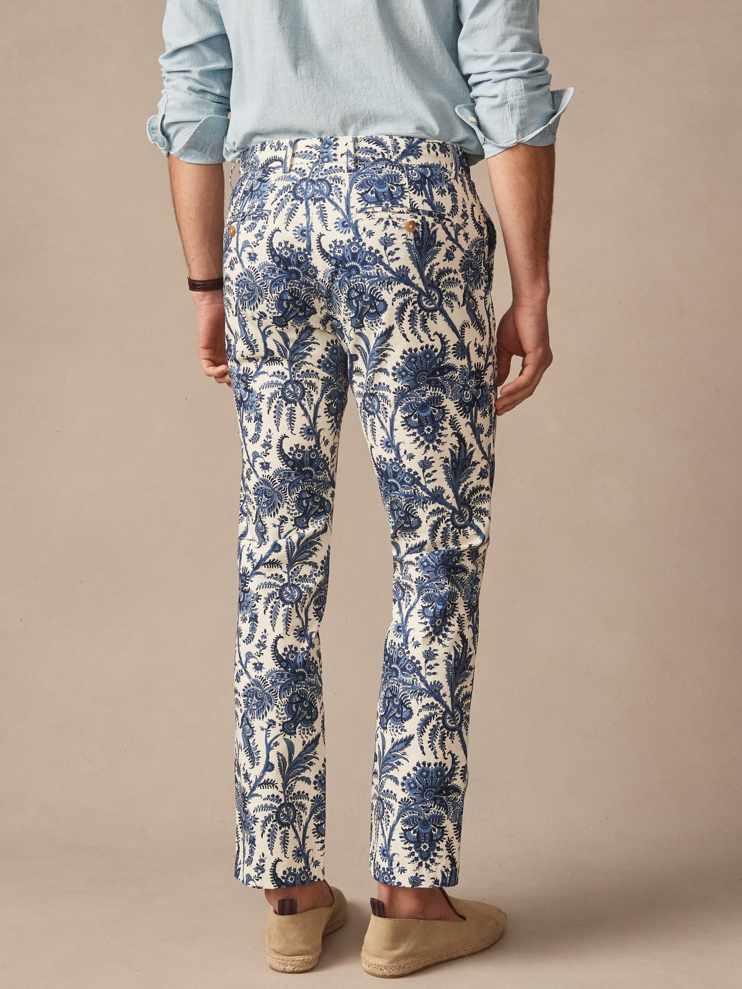 Man wearing Madison Fancy Pants in Heirloom Paisley by J.McLaughlin, featuring an intricate cream and navy pattern, paired with a light blue shirt and casual slip-on shoes, showcasing effortlessly stylish design and enduring craftsmanship. A destination for defining style. Life, Well-Lived.