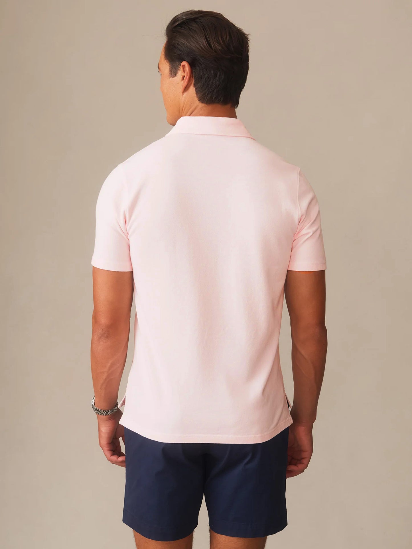 Man wearing a pale pink Mantle Pique Polo by J.McLaughlin paired with navy shorts, showcasing effortlessly stylish and enduring design in a classic fit.