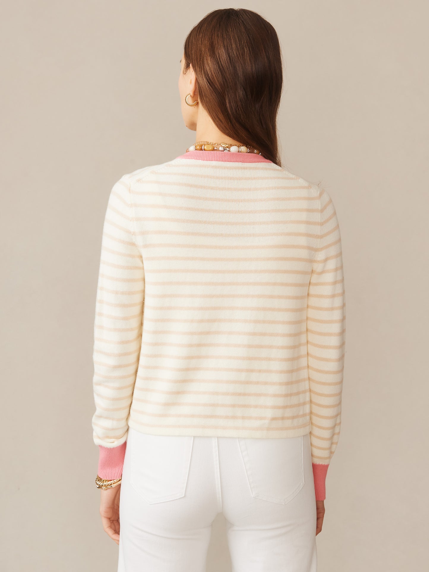 A rear view of a woman wearing the Matilda Cardigan in Stripe by J.McLaughlin, featuring soft neutral stripes with pink accents at the collar and cuffs, effortlessly stylish for enduring designs in versatile sweaters.