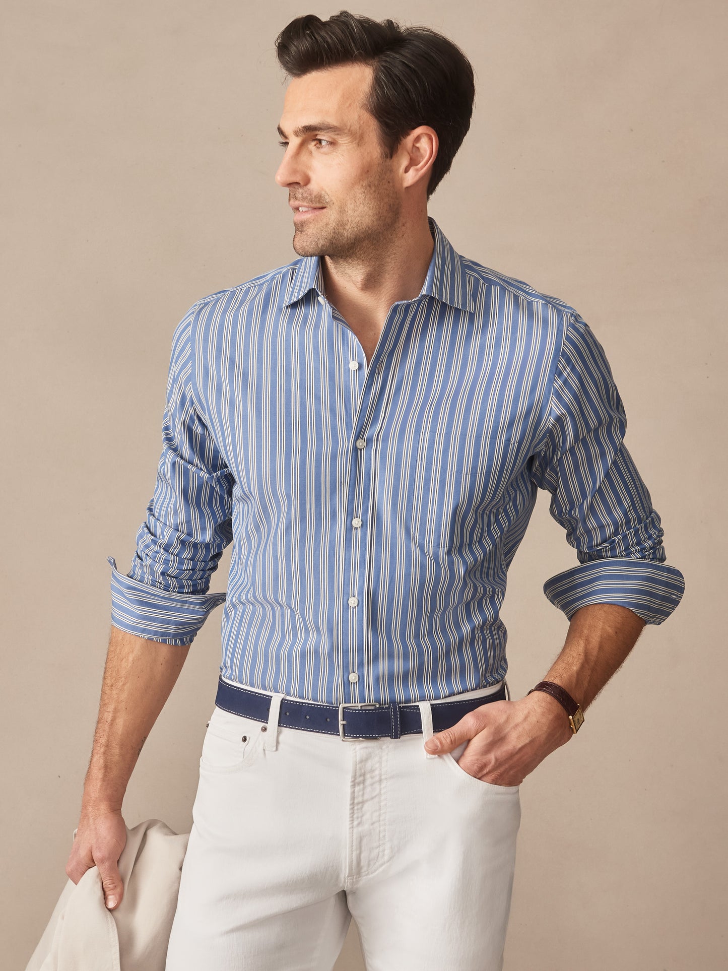 Man wearing a Gramercy Cotton Shirt in Varigated Stripe by J.McLaughlin, paired with white pants and a navy belt, showcasing effortlessly stylish, enduring designs in timeless fashion.