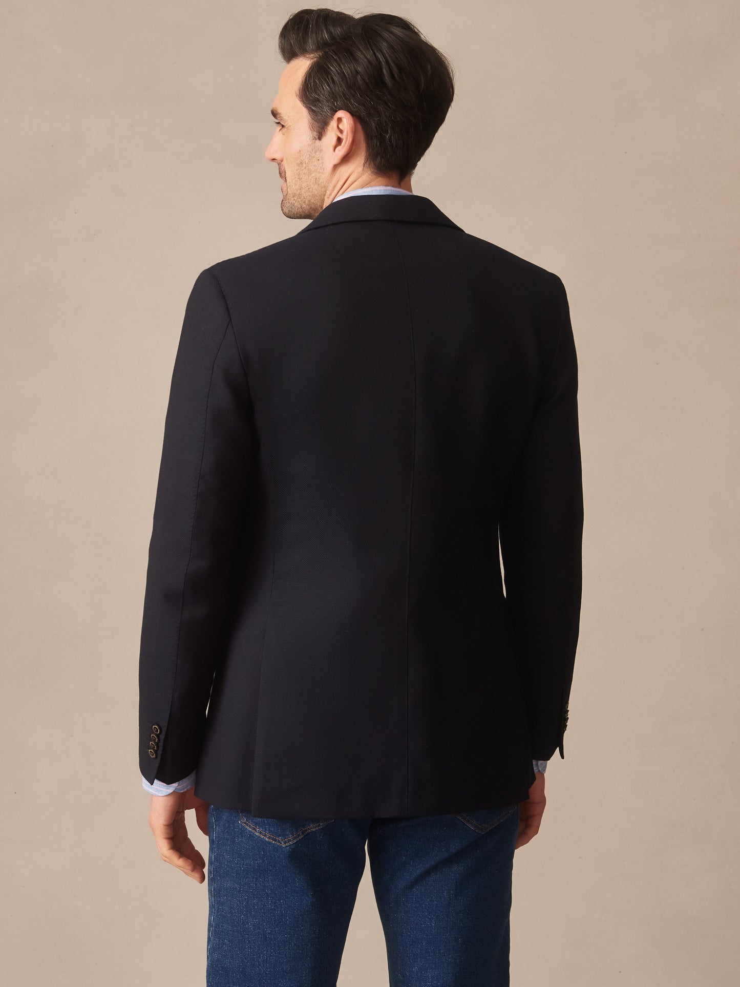 Man wearing a navy Suffolk Sport Coat by J.McLaughlin paired with denim jeans, showcasing effortlessly stylish, enduring designs and innovative fabrics for a legacy of timeless fashion.