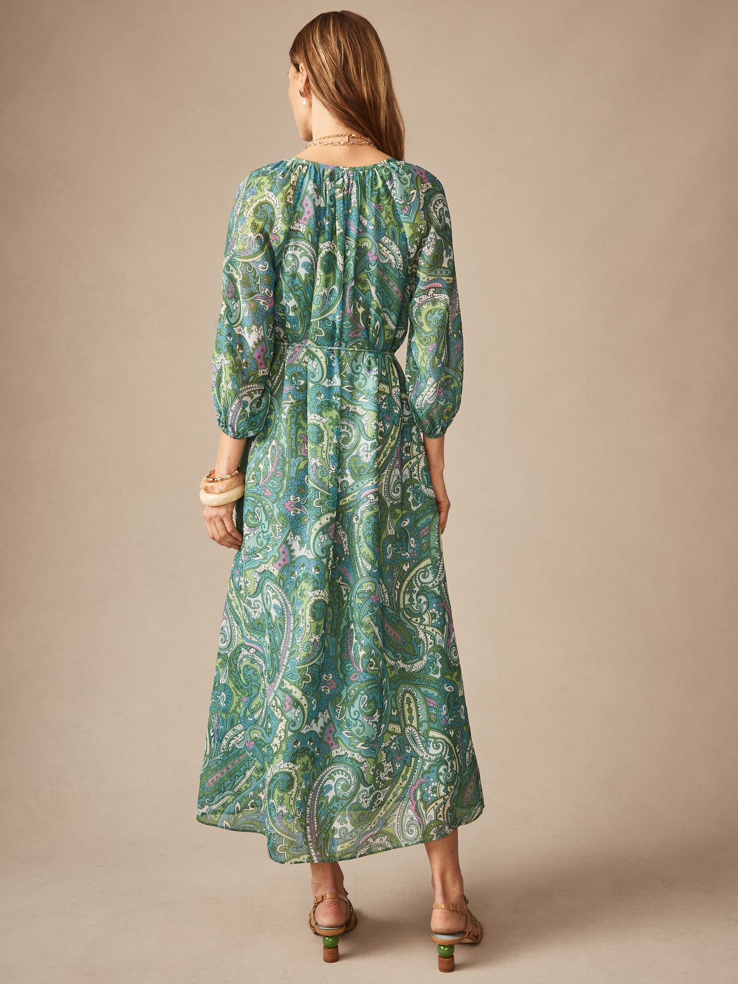 Woman wearing Mia Dress in Paisley Reverie by J.McLaughlin featuring a flowing paisley pattern in blue and green hues, paired with sandals and bracelets, showcasing effortlessly stylish, enduring designs and a legacy of timeless fashion. A destination for defining style. Life, Well-Lived.