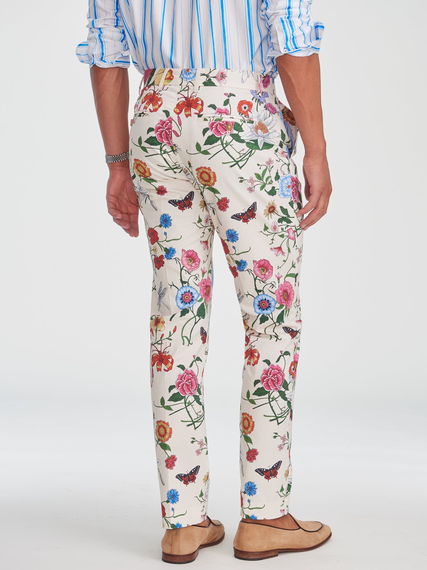 Back view of a man wearing J.McLaughlin Madison Fancy Pants in Dragonfly Garden, featuring a vibrant floral and butterfly print on cream fabric, paired with leather shoes and a blue striped shirt. Effortlessly stylish, with enduring designs and innovative fabrics—a destination for defining style. Life, Well-Lived.