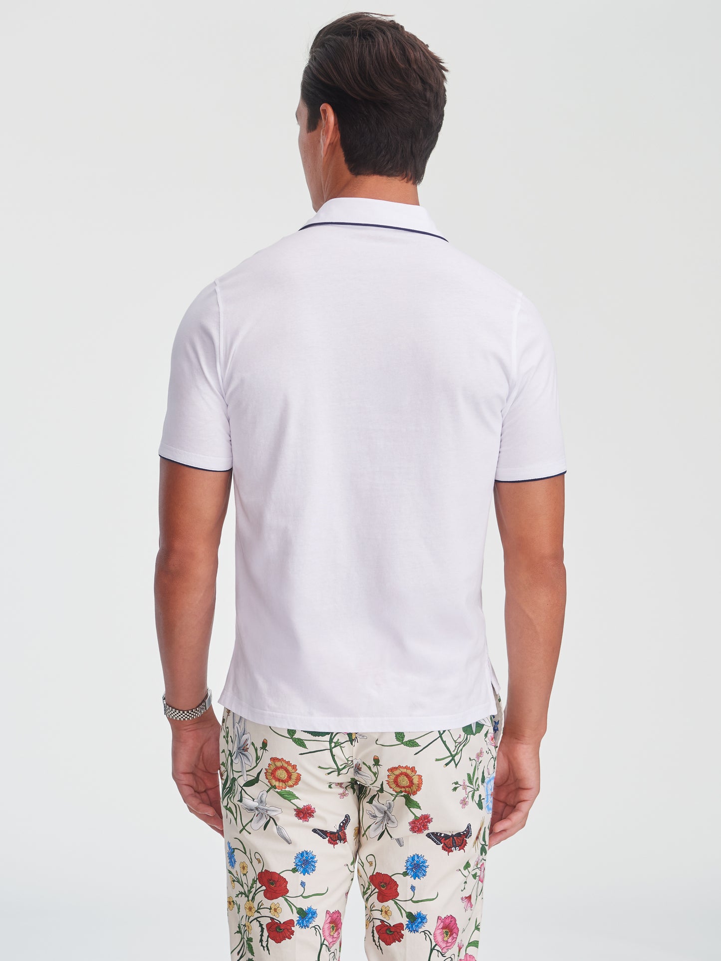Man wearing a white Ryan Polo by J.McLaughlin paired with floral print pants, showcasing effortlessly stylish and enduring designs in innovative fabrics, a destination for defining style. Life, Well-Lived.
