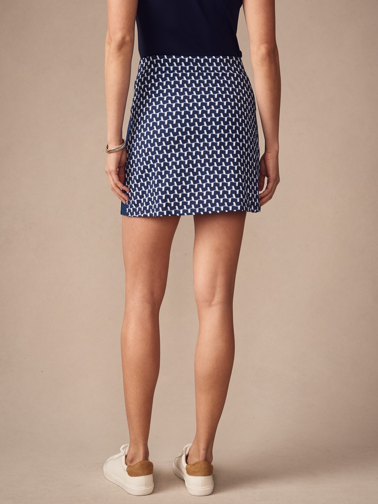 Back view of a woman wearing a navy and light blue patterned Palm Springs Skort in Duncan by J.McLaughlin, paired with white sneakers, showcasing effortlessly stylish, enduring designs and innovative fabrics.
