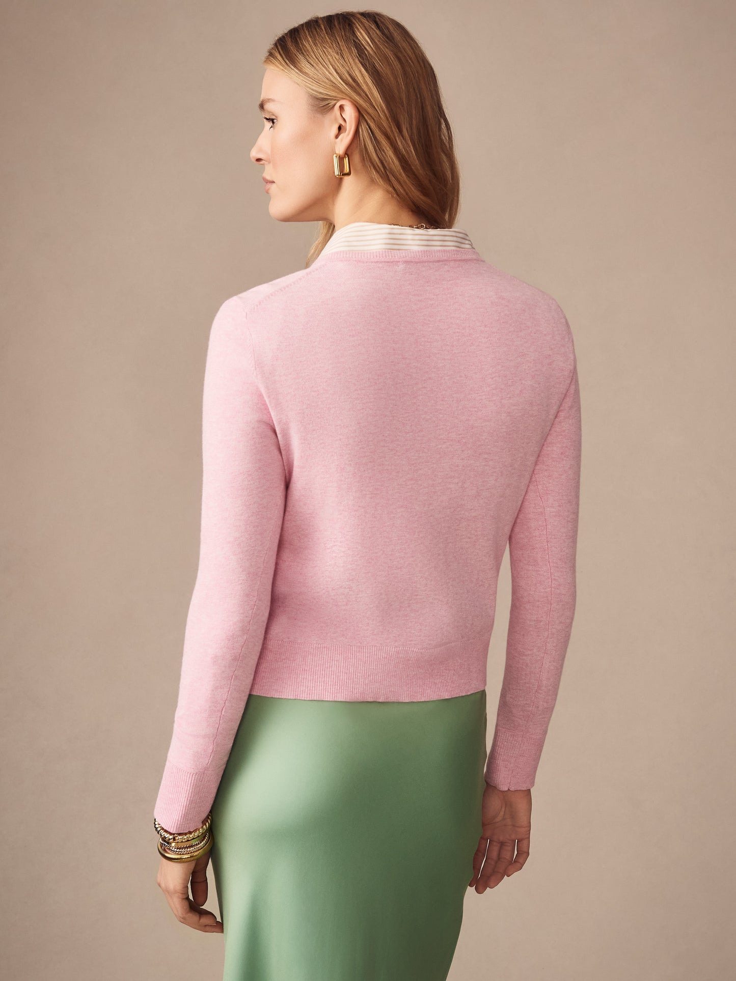 Woman wearing a pink Pearl Cardigan by J.McLaughlin paired with a green skirt, showcasing effortlessly stylish and enduring designs crafted from innovative fabrics.