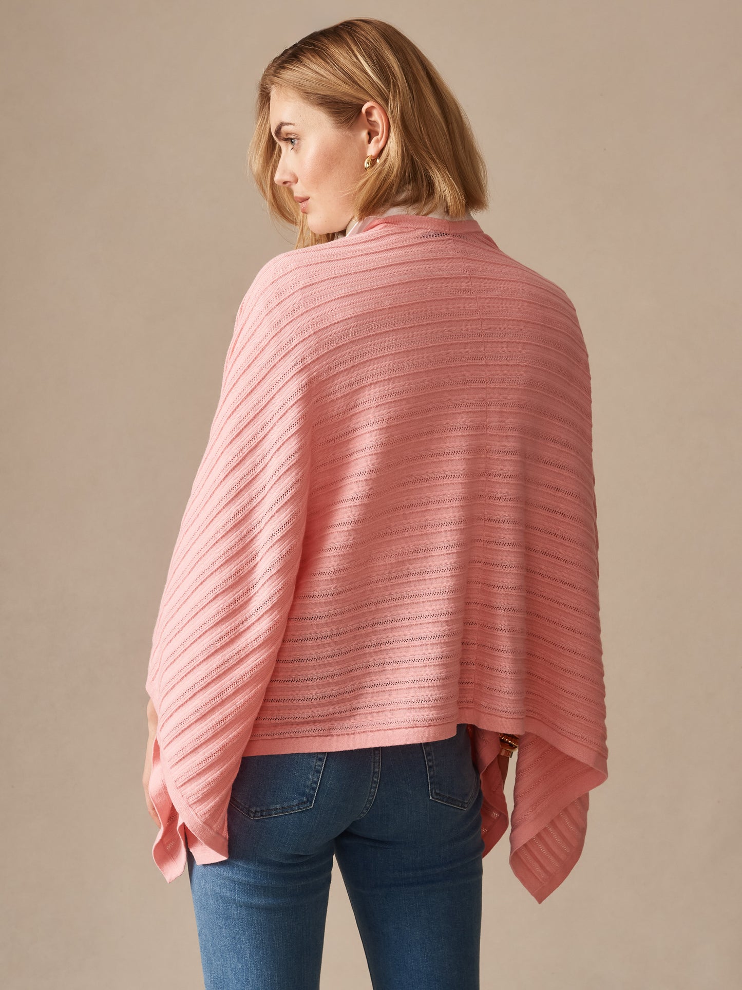 A woman wearing a coral pink Penny Wrap from J.McLaughlin, showcasing effortlessly stylish, enduring designs in a lightweight, textured fabric, perfect for timeless layering.