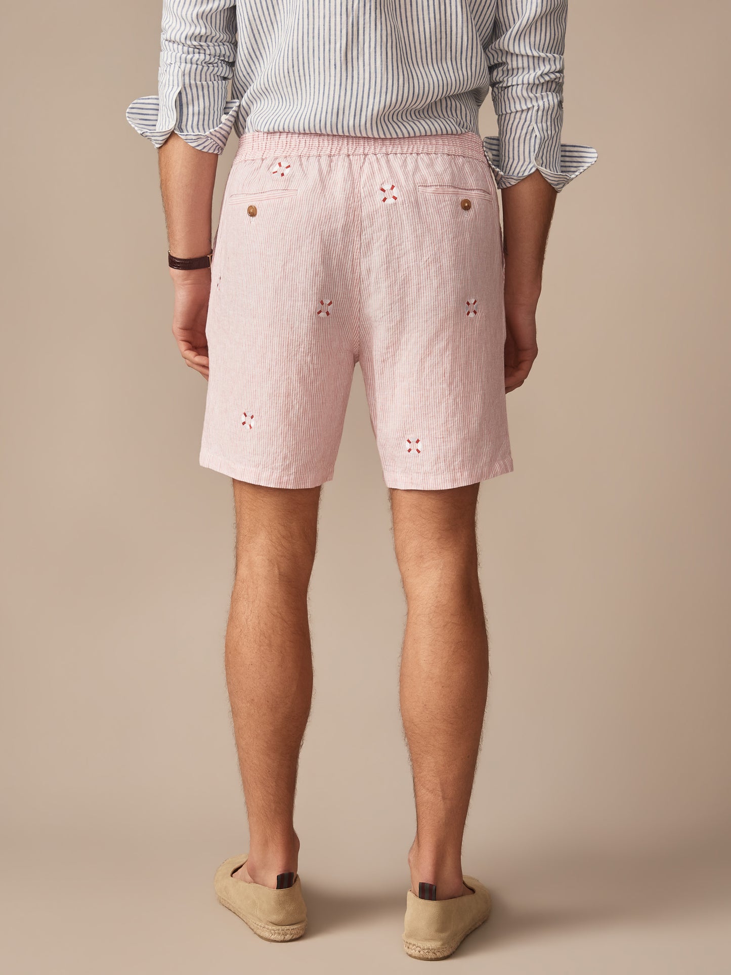 Men's back view wearing pink lightweight Newport Linen Shorts in Lifesaver by J.McLaughlin, paired with a striped shirt and casual slip-on shoes, embodying effortlessly stylish, enduring designs.