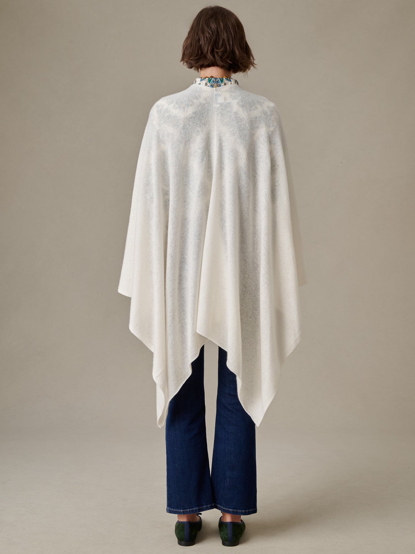 Back view of a model wearing a white Rossi Cashmere Wrap by J.McLaughlin over blue jeans and black shoes, showcasing an effortlessly stylish and timeless design.