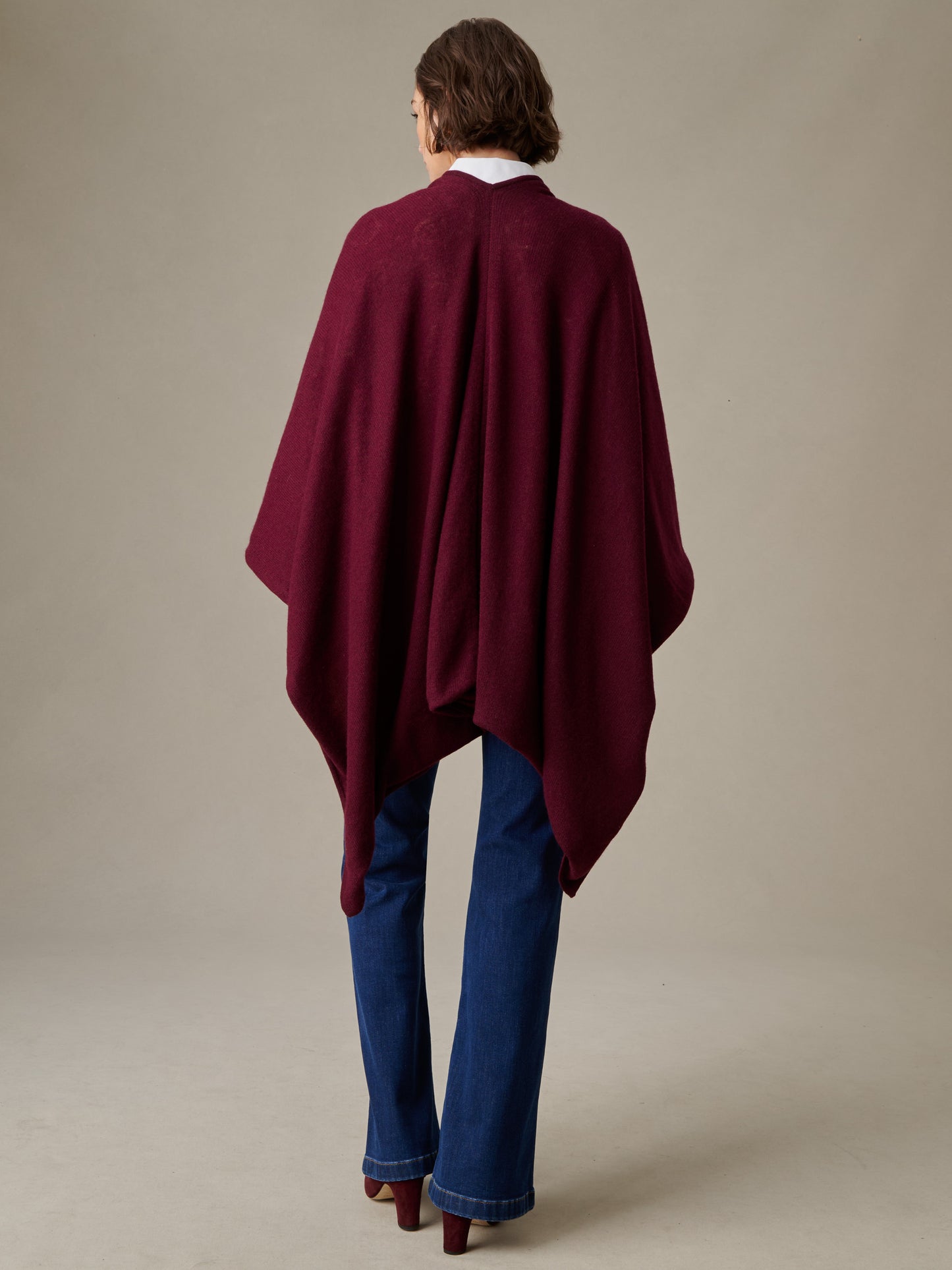 Woman wearing a deep burgundy Rossi Cashmere Wrap in Grand Heraldic Border over blue jeans and heels, showcasing timeless style and luxurious craftsmanship by J.McLaughlin.