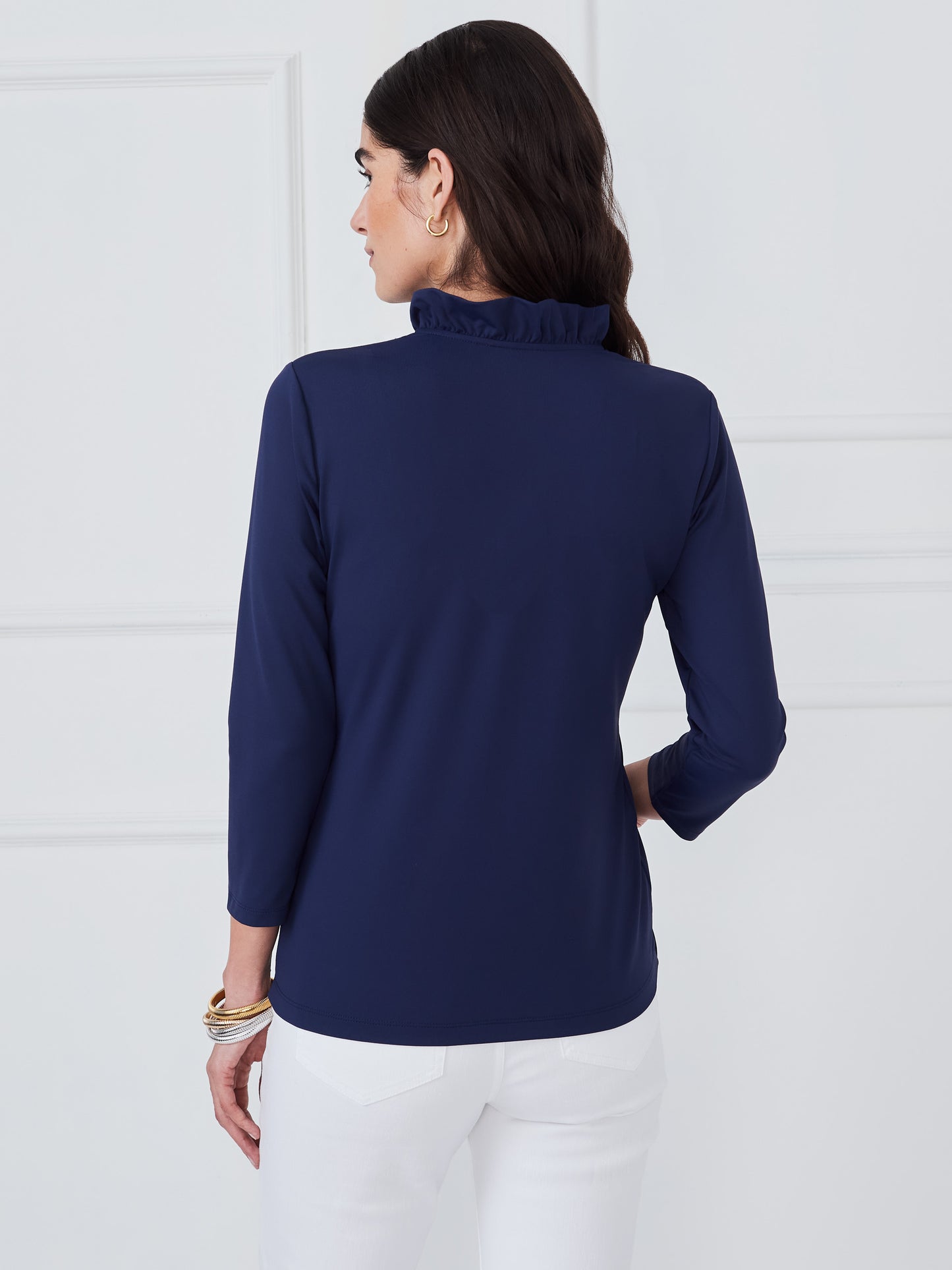 Woman wearing a navy Kate Ruffle Top by J.McLaughlin, showcasing effortless style with a ruffled neckline and long sleeves, embodying enduring designs and a legacy of timeless fashion. A destination for defining style. Life, Well-Lived.