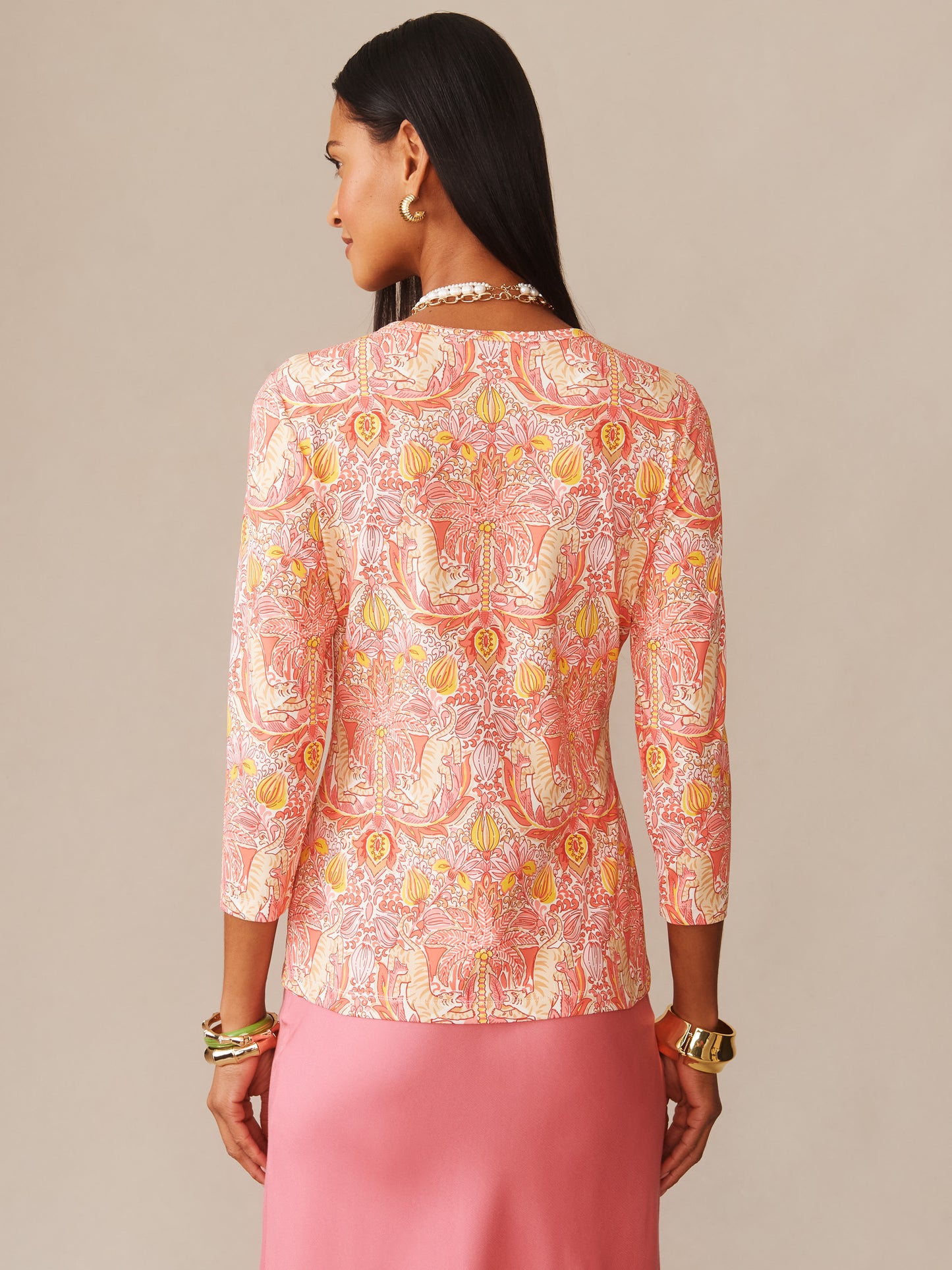 Woman wearing the Signature Tee in Tigress Tropico by J.McLaughlin, featuring an intricate coral pink patterned top with three-quarter sleeves paired with a pink skirt, showcasing effortlessly stylish, enduring designs and a legacy of timeless fashion. A destination for defining style. Life, Well-Lived.