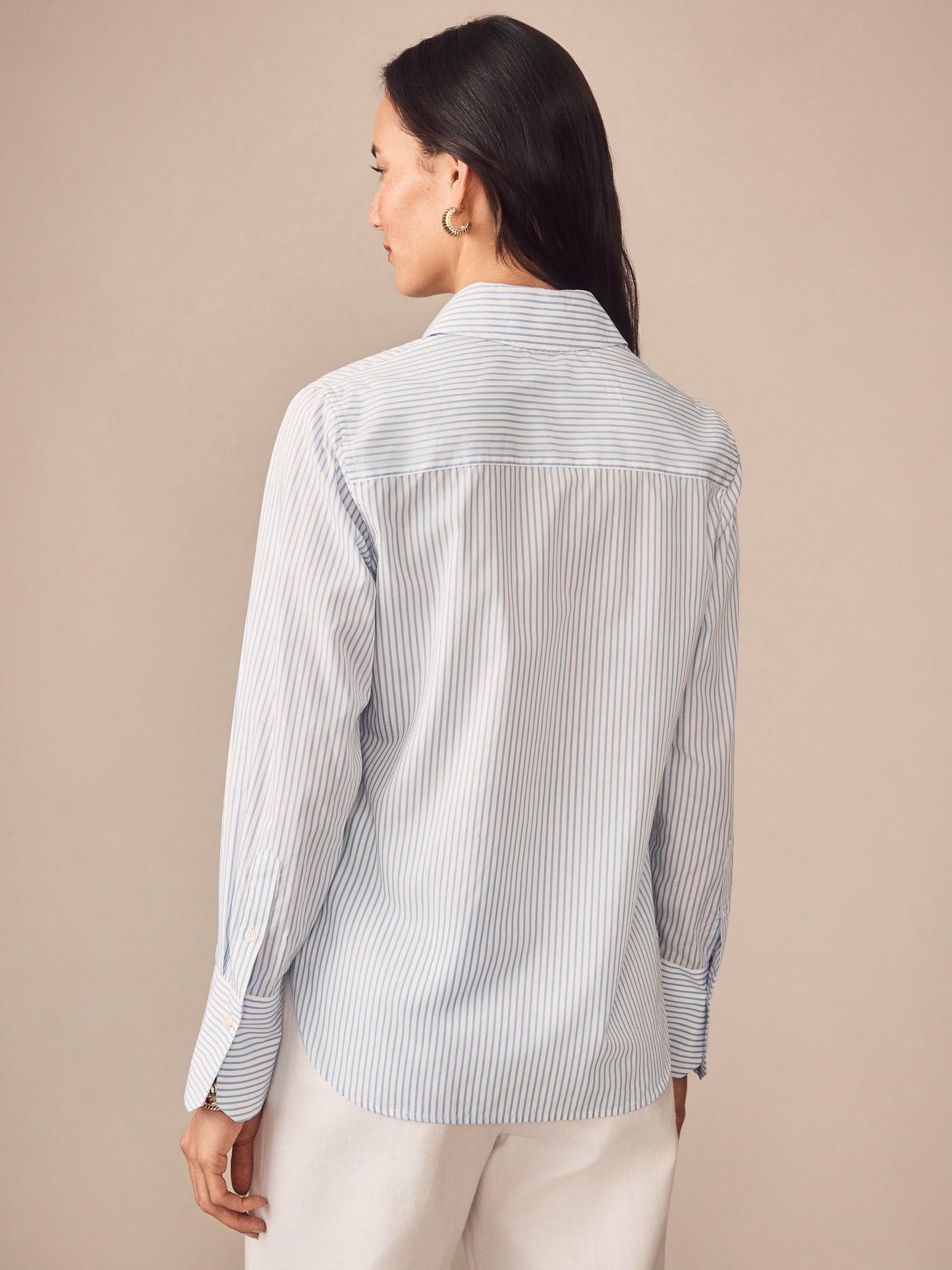 Woman wearing a J.McLaughlin Sloane Shirt in Stripe, featuring soft blue and white stripes, embodying effortlessly stylish, enduring designs and innovative fabrics for a life well-lived.