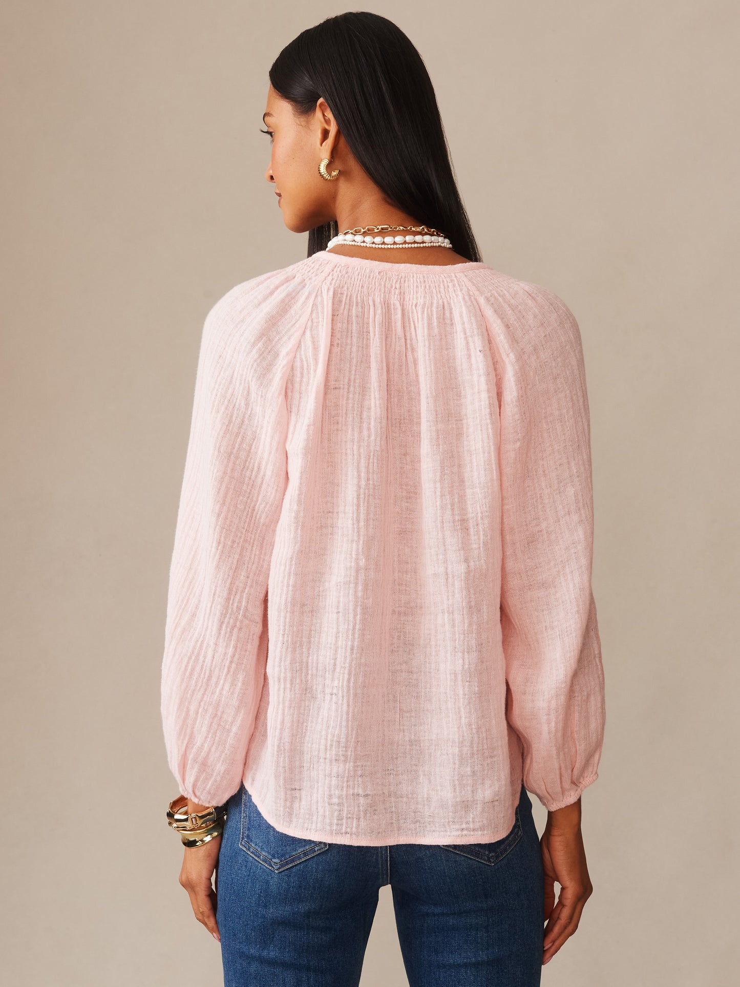 Woman wearing a soft pink Tatiana Linen Blouse by J.McLaughlin, styled with pearl necklace and gold earrings, showcasing effortlessly stylish, enduring designs.
