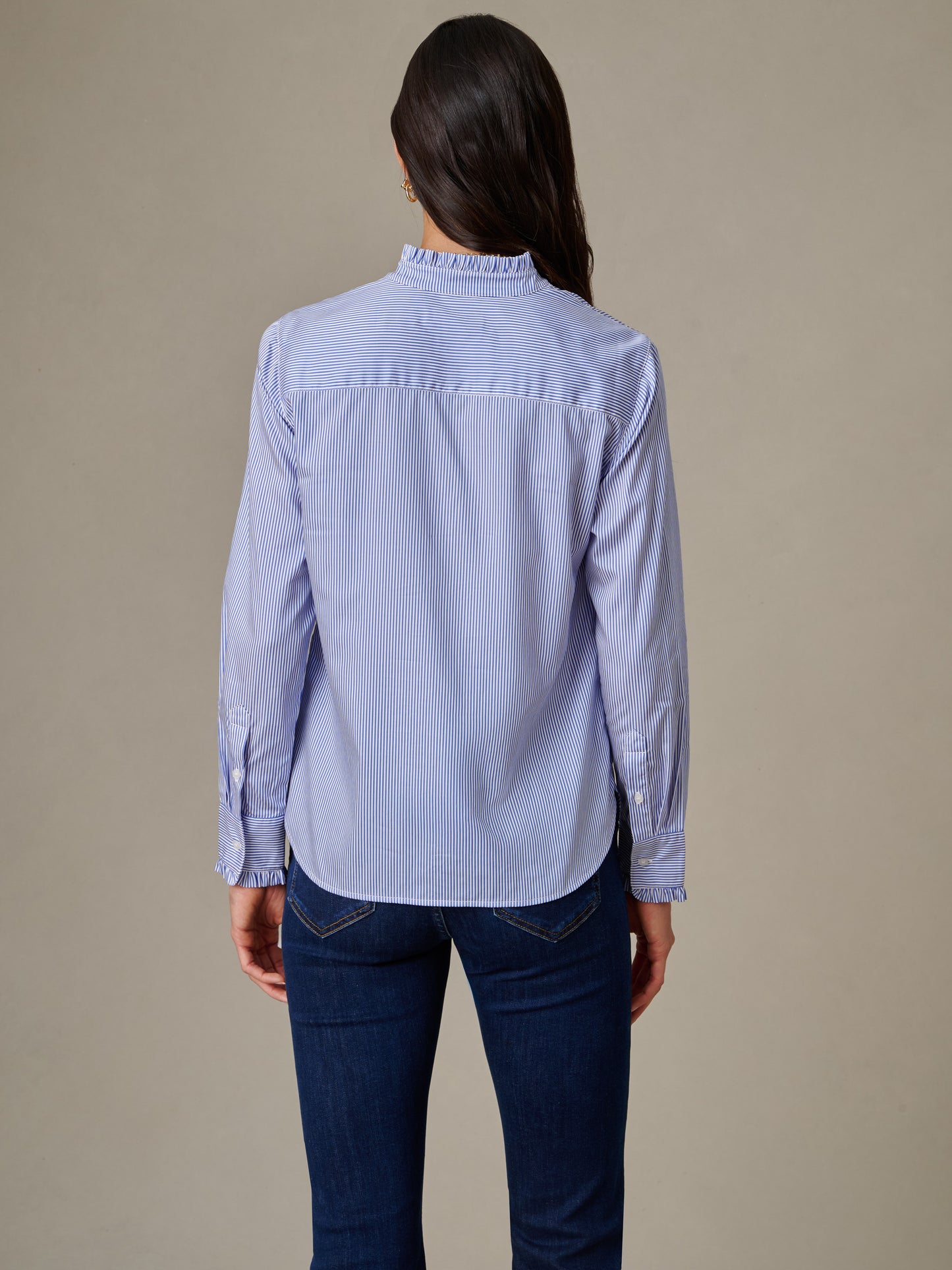 Woman wearing a J.McLaughlin Tess Ruffle Collar Shirt in Stripe, featuring a light blue striped pattern with a ruffled collar, paired with dark blue jeans.