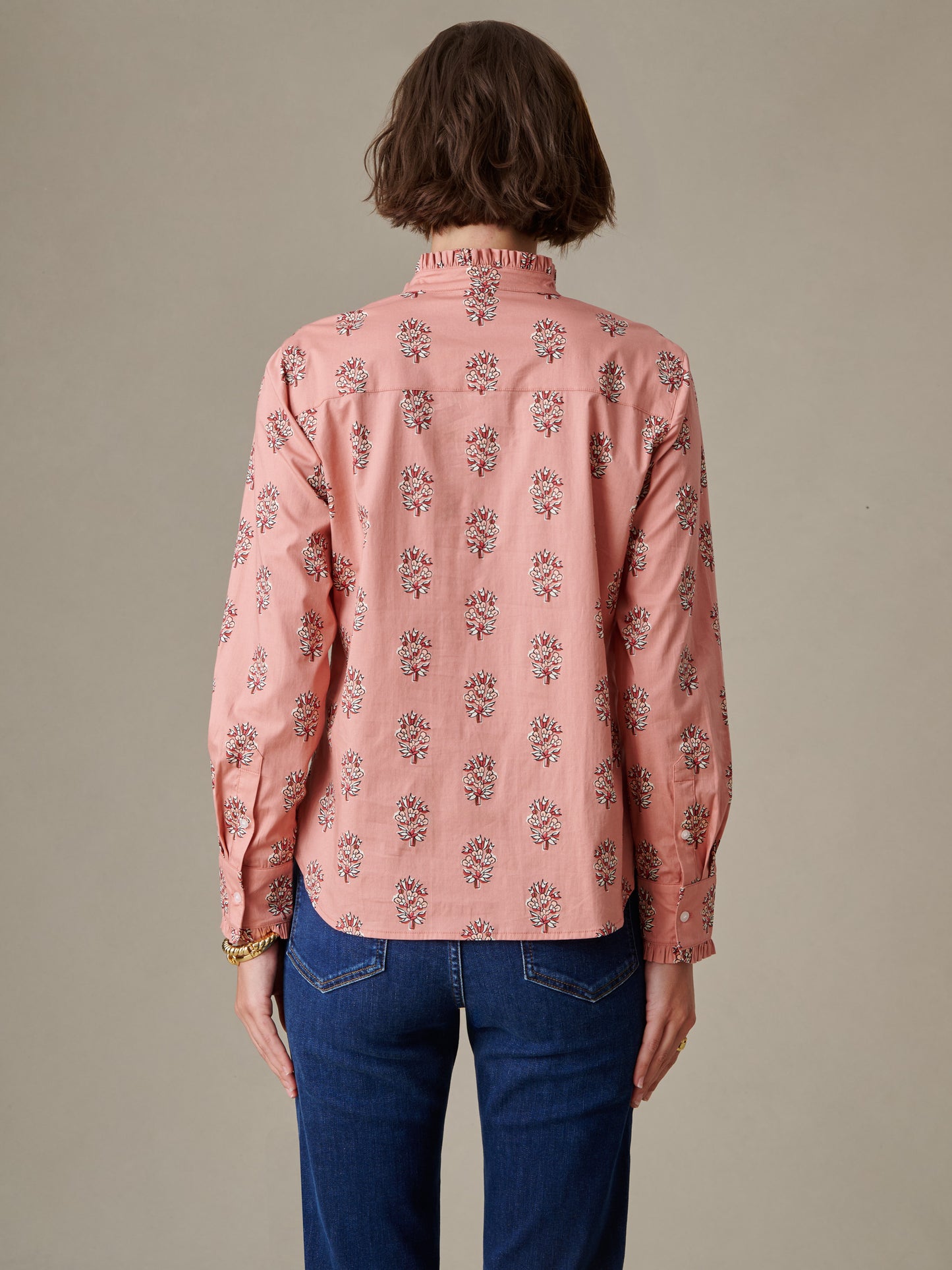 Woman seen from behind wearing the Tess Ruffle Collar Shirt in Heritage Bloom by J.McLaughlin, featuring a soft pink floral pattern and ruffled collar detail paired with blue jeans.