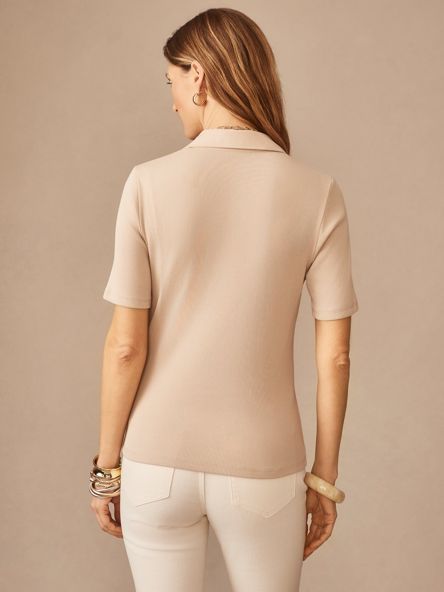 Woman wearing Theodora Short Sleeve Shirt in a soft almond color, styled with white pants and gold-tone bracelets, showcasing J.McLaughlin’s effortlessly stylish, enduring design.