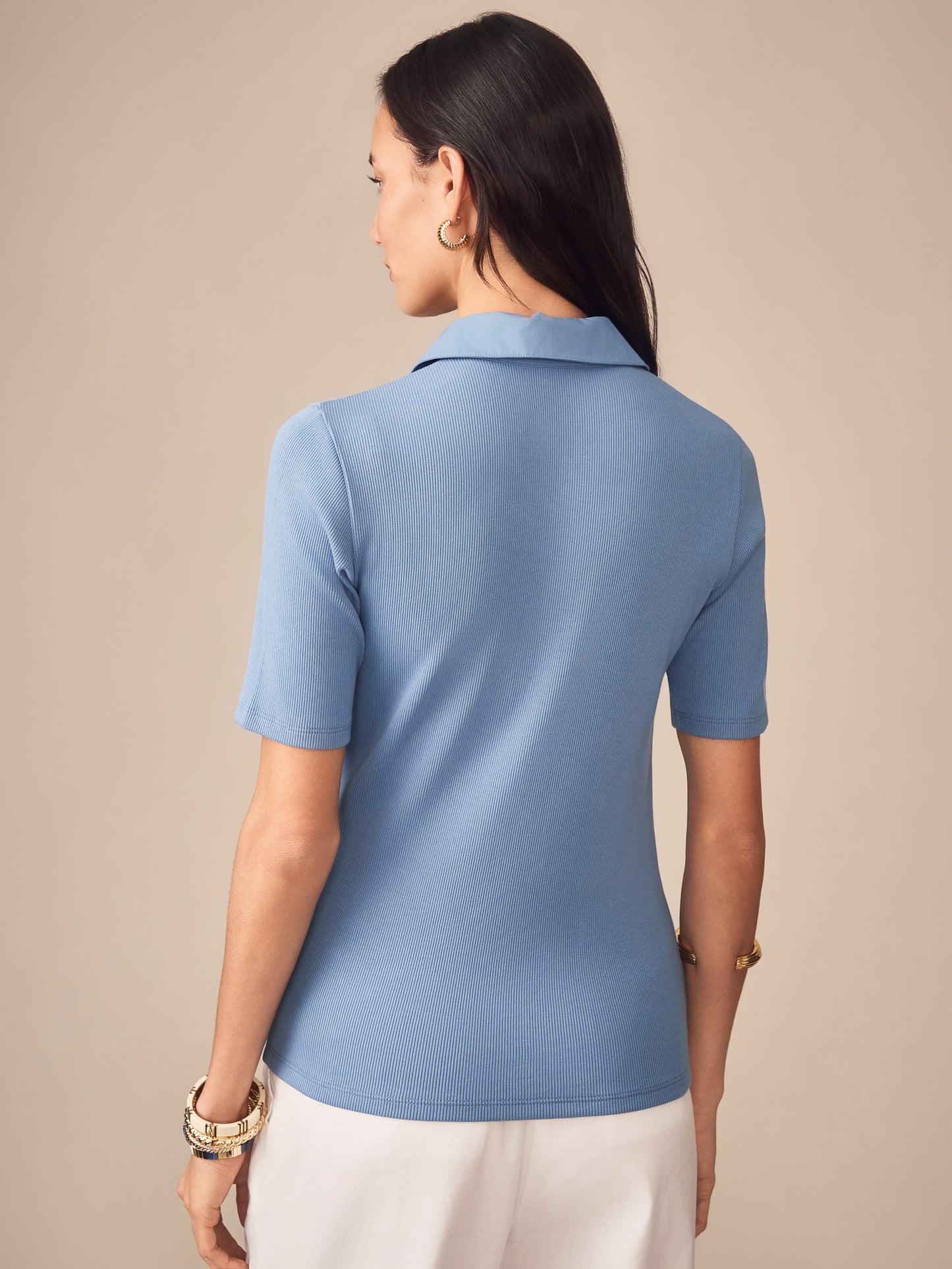 A rear view of a woman wearing the Theodora Short Sleeve Shirt in a soft seaside blue by J.McLaughlin, showcasing effortlessly stylish, enduring designs crafted with innovative fabrics for a legacy of timeless fashion. A destination for defining style. Life, Well-Lived.