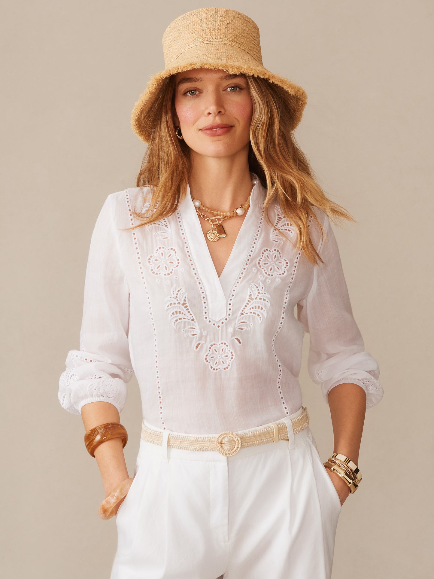 Woman wearing an effortlessly stylish Anna Straw Hat by J.McLaughlin, paired with a white embroidered blouse and accessories, showcasing enduring designs and a legacy of timeless fashion.
