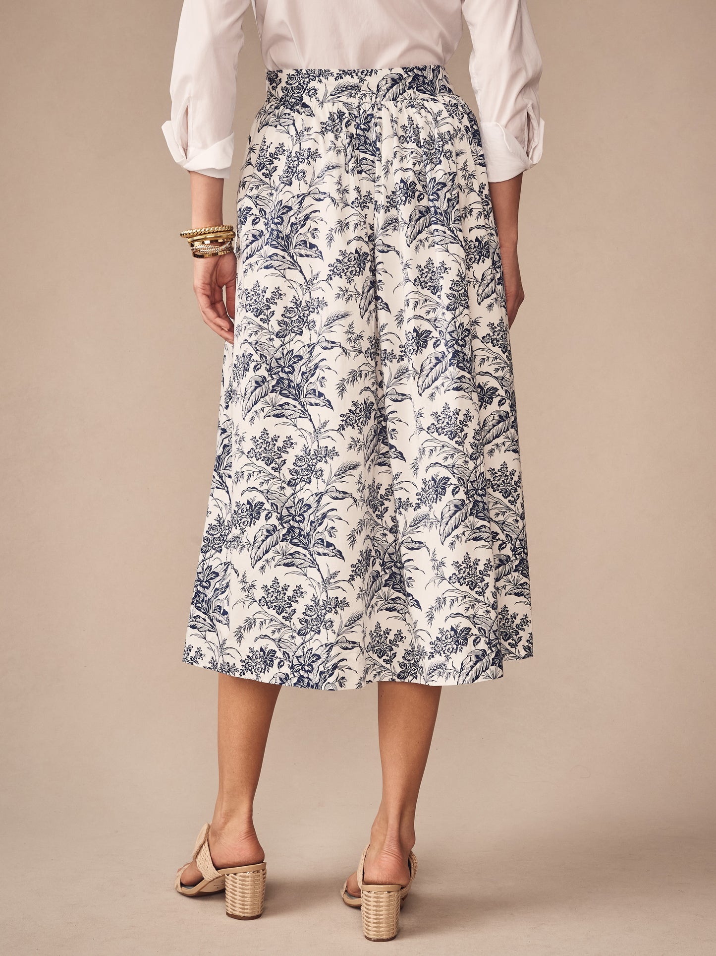 Back view of a woman wearing the Winnie Skirt in Giardino Toile by J.McLaughlin, featuring a navy floral pattern on white fabric paired with a white blouse and block heel sandals, embodying effortlessly stylish, enduring designs from a destination for defining style. Life, Well-Lived.