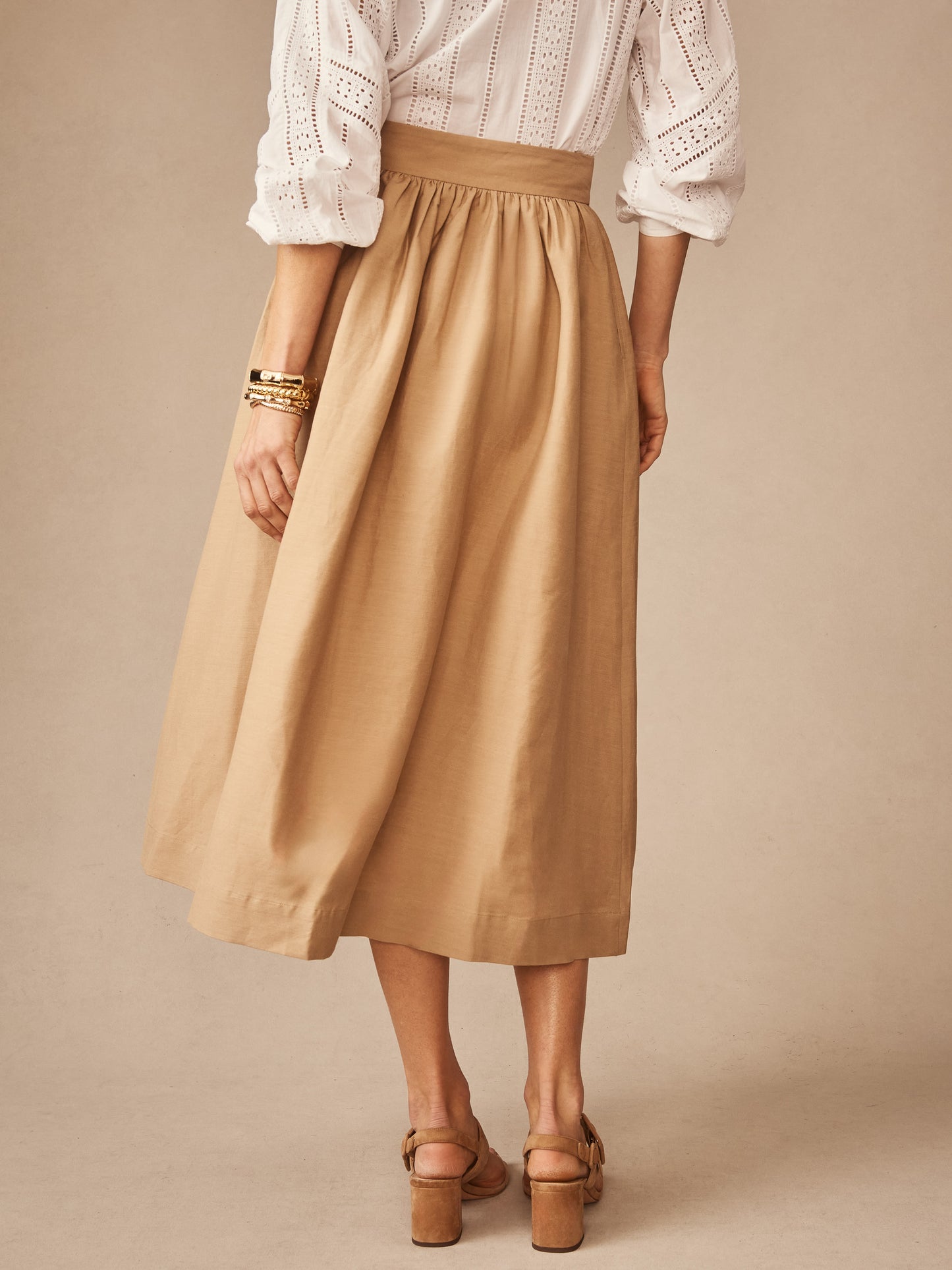 Rear view of a woman wearing a khaki Winnie Linen Blend Skirt paired with a white eyelet blouse, showcasing J. McLaughlin’s effortlessly stylish, enduring designs and innovative fabrics.