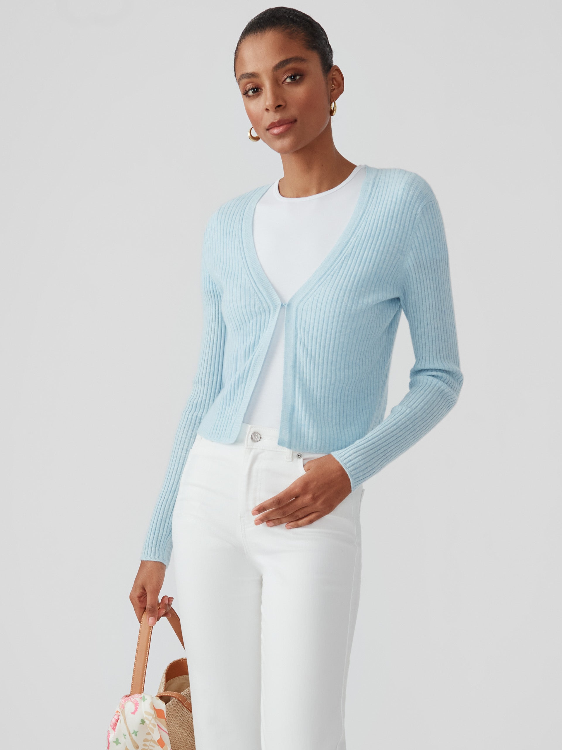 Woman wearing a baby blue Imogen Cashmere Cardigan by J.McLaughlin paired with white pants, showcasing effortlessly stylish, enduring designs and a legacy of timeless fashion.