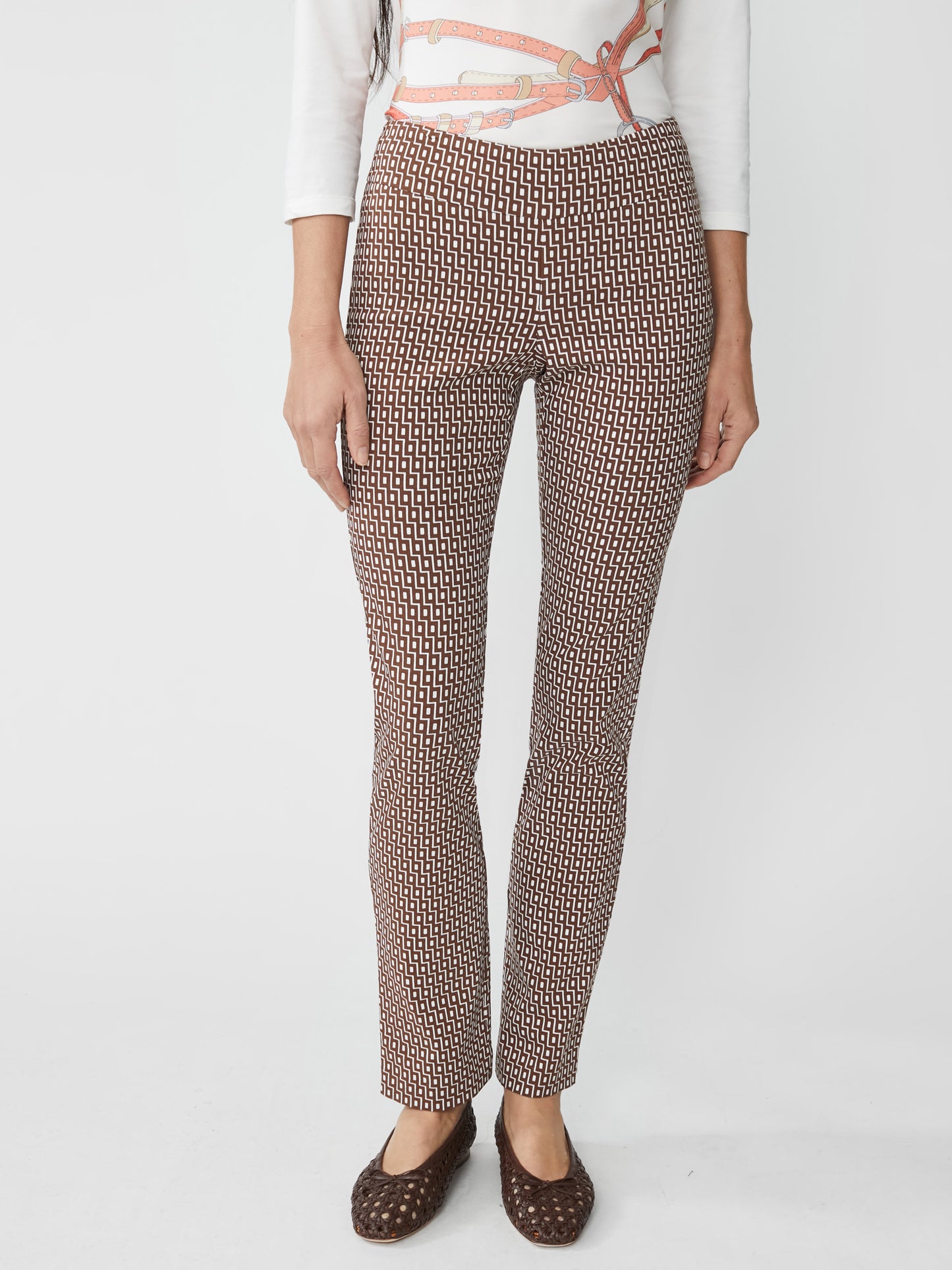 A front view of a woman wearing Masie Pants in Micro City Windows by J.McLaughlin, featuring a brown and off-white geometric pattern, paired with a stylish white top and brown woven flats, embodying effortlessly stylish, enduring designs, innovative fabrics, and a legacy of timeless fashion—a destination for defining style. Life, Well-Lived.