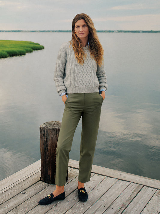 Woman standing on a dock wearing Avery Cotton Chino Pants by J.McLaughlin paired with a cozy gray sweater and black loafers, embodying effortlessly stylish, enduring designs.