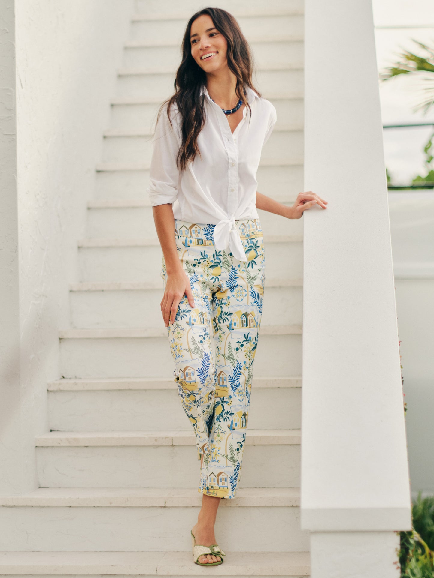 Woman wearing J.McLaughlin Ivy Pants in Amalfi Coast with a white tied shirt and sandals, showcasing effortlessly stylish, enduring designs and innovative fabrics.