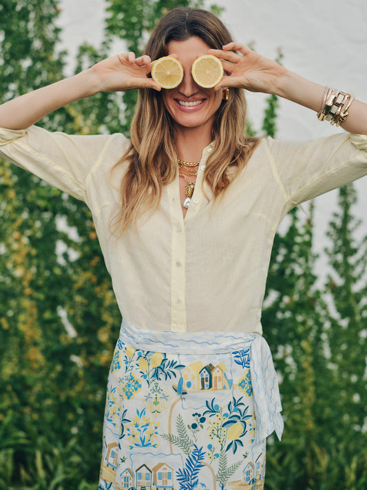 Woman wearing a Britt Linen Shirt by J.McLaughlin in soft yellow, playfully holding lemon halves over her eyes, showcasing effortlessly stylish, enduring designs.