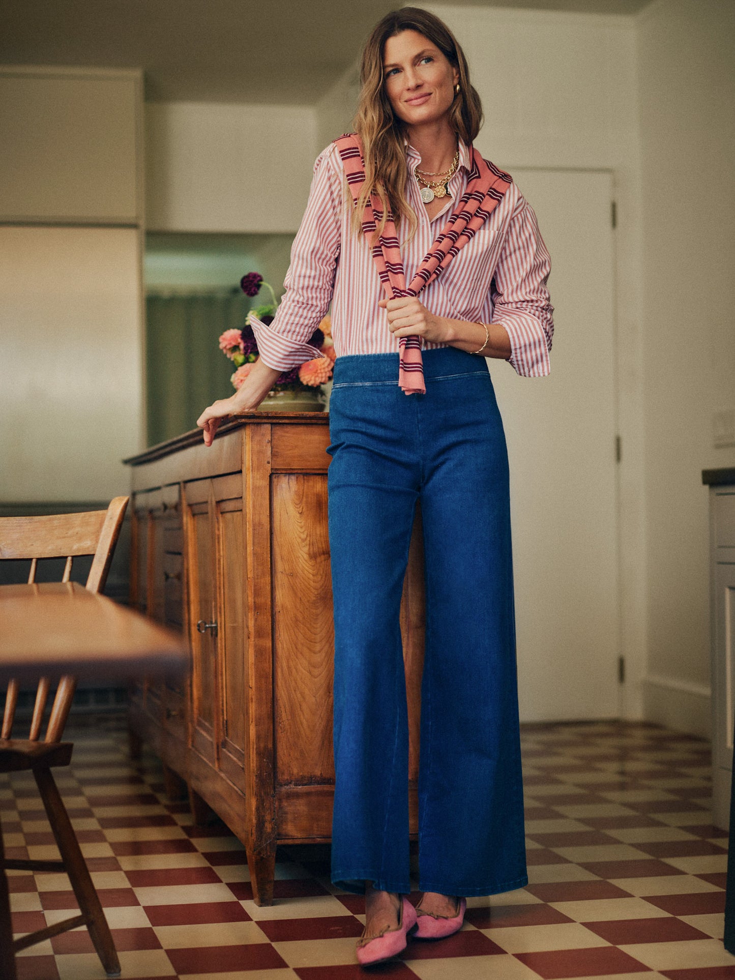 Woman wearing Anderson Jeans by J.McLaughlin paired with a striped blouse and pink sweater, showcasing effortlessly stylish and enduring designs in a cozy indoor setting.
