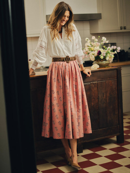 Woman wearing an Arabella Skirt in Heritage Bloom Cross by J.McLaughlin, paired with a white blouse and leopard print belt, standing in a classic kitchen with floral decor.