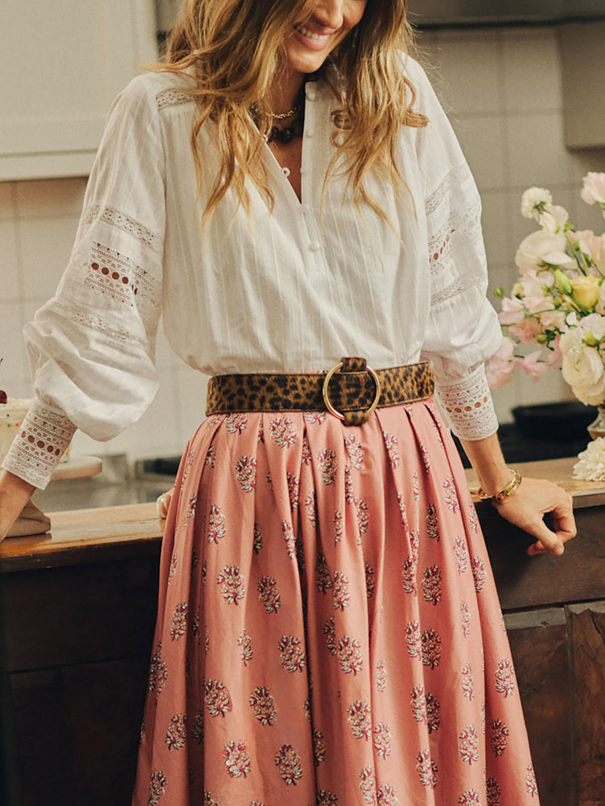 Woman wearing a white blouse and pink floral skirt cinched at the waist with an Amelia Pony Hair Belt in Leopard by J.McLaughlin, showcasing timeless style and quality craftsmanship.