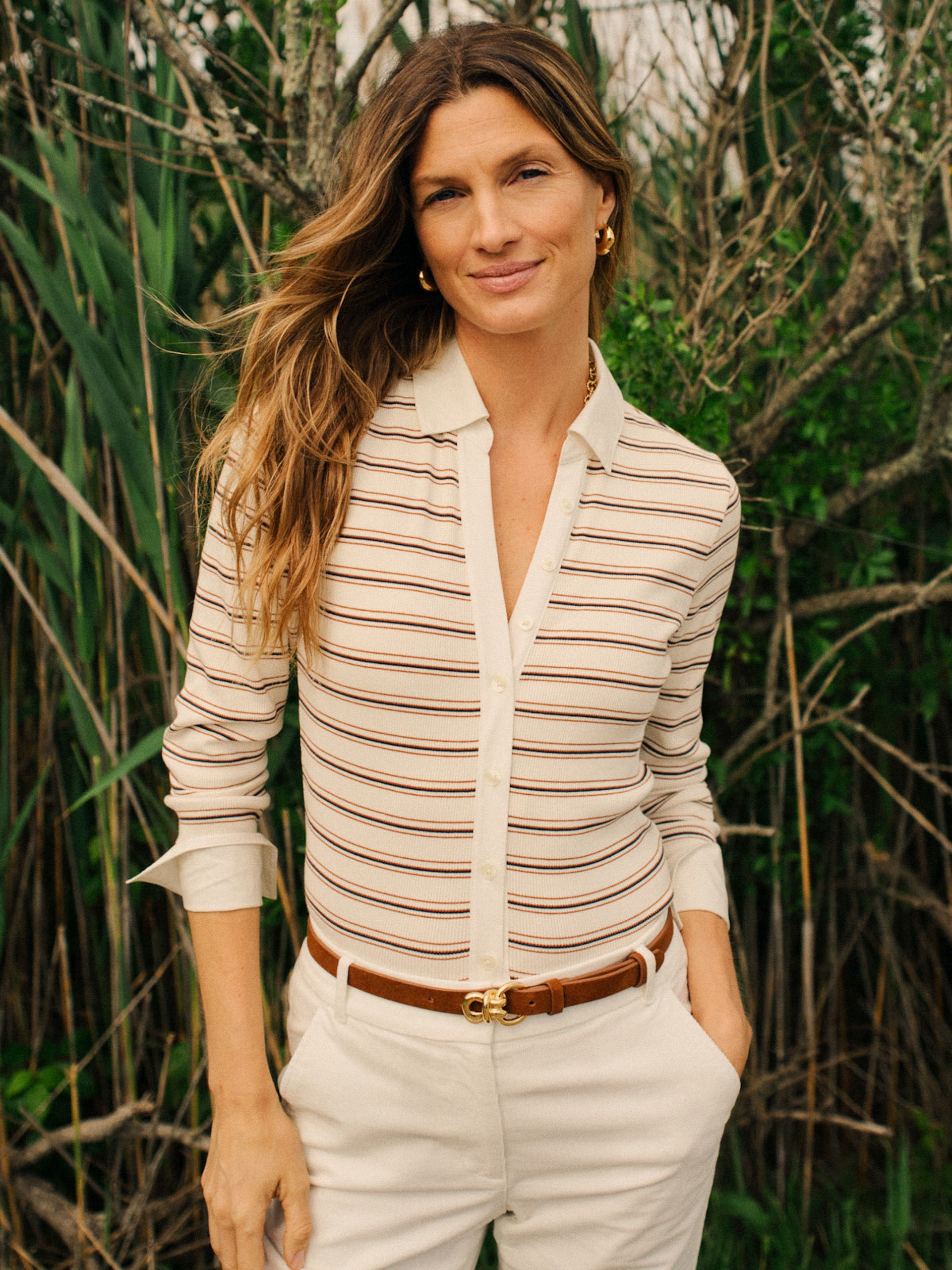 Woman outdoors wearing Theodora Shirt in Stripe by J.McLaughlin, styled with light pants and a brown belt, showcasing effortlessly stylish and timeless design.