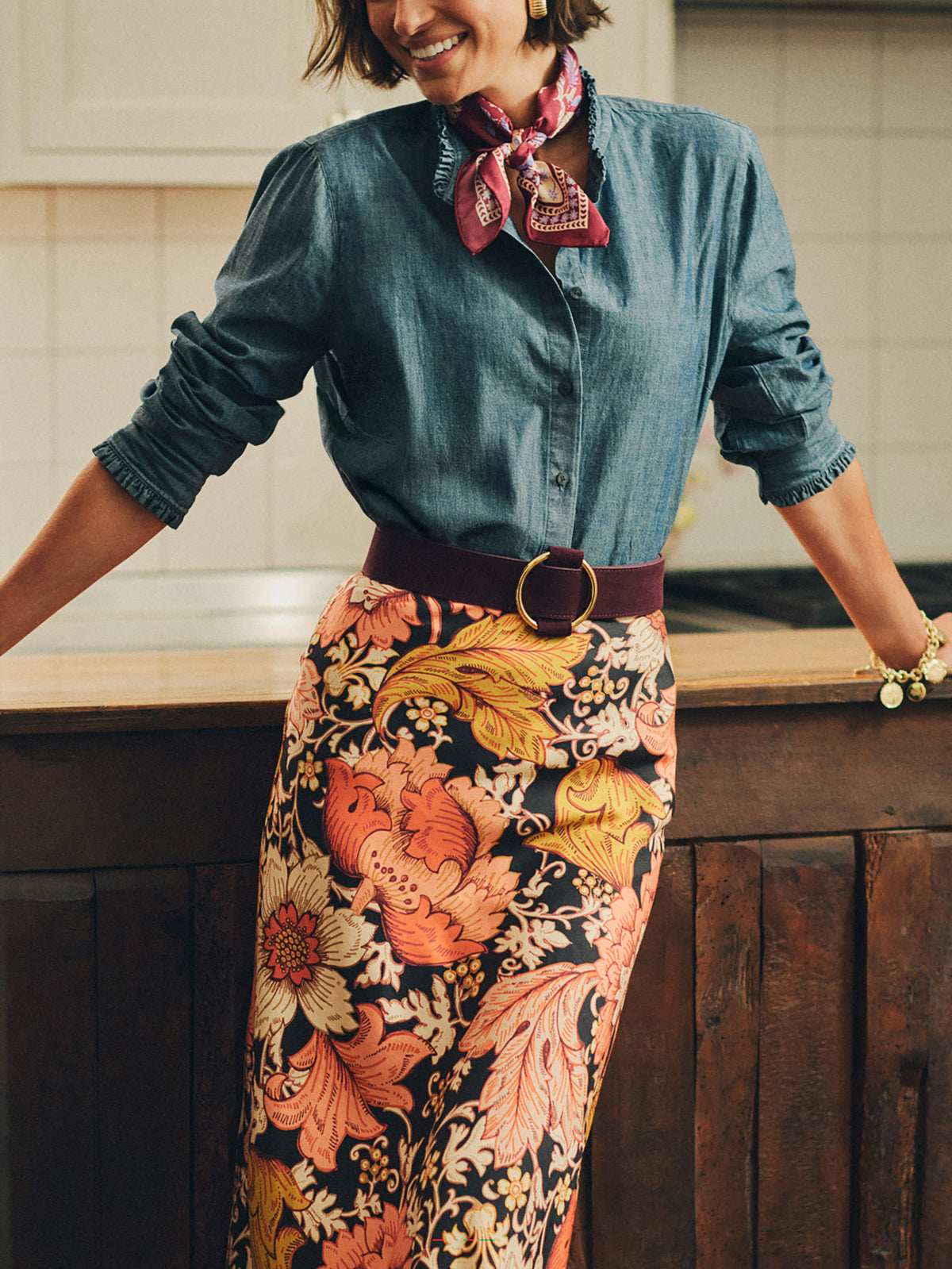 Woman wearing a denim shirt and floral skirt cinched at the waist with an Amelia Suede Belt by J.McLaughlin, showcasing enduring style and effortless elegance.