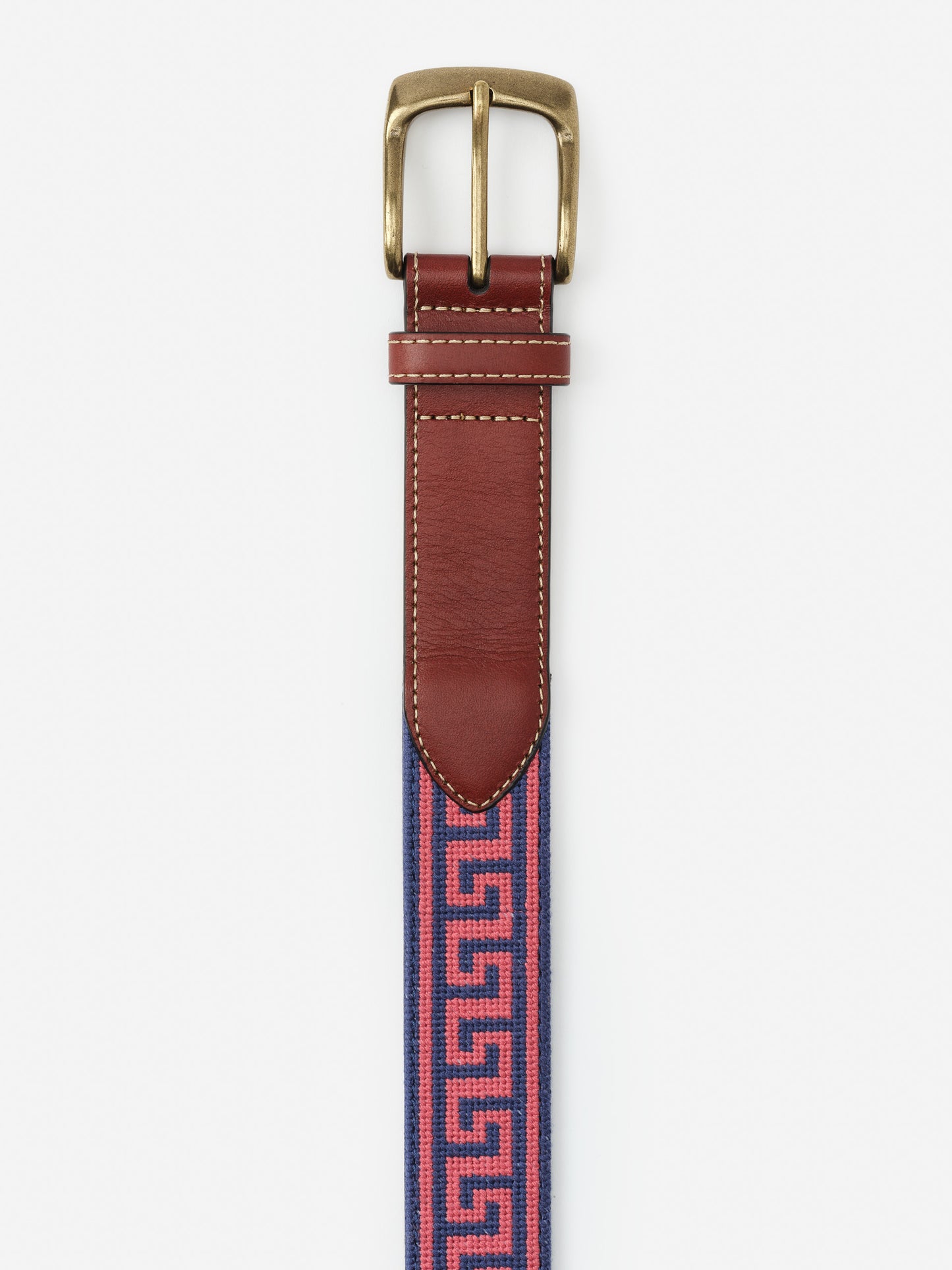 Close-up of the top half of a Needlepoint Belt in Greek Key by J.McLaughlin, featuring a brass buckle, rich brown leather trim, and a pink and navy needlepoint pattern with a Greek key design.