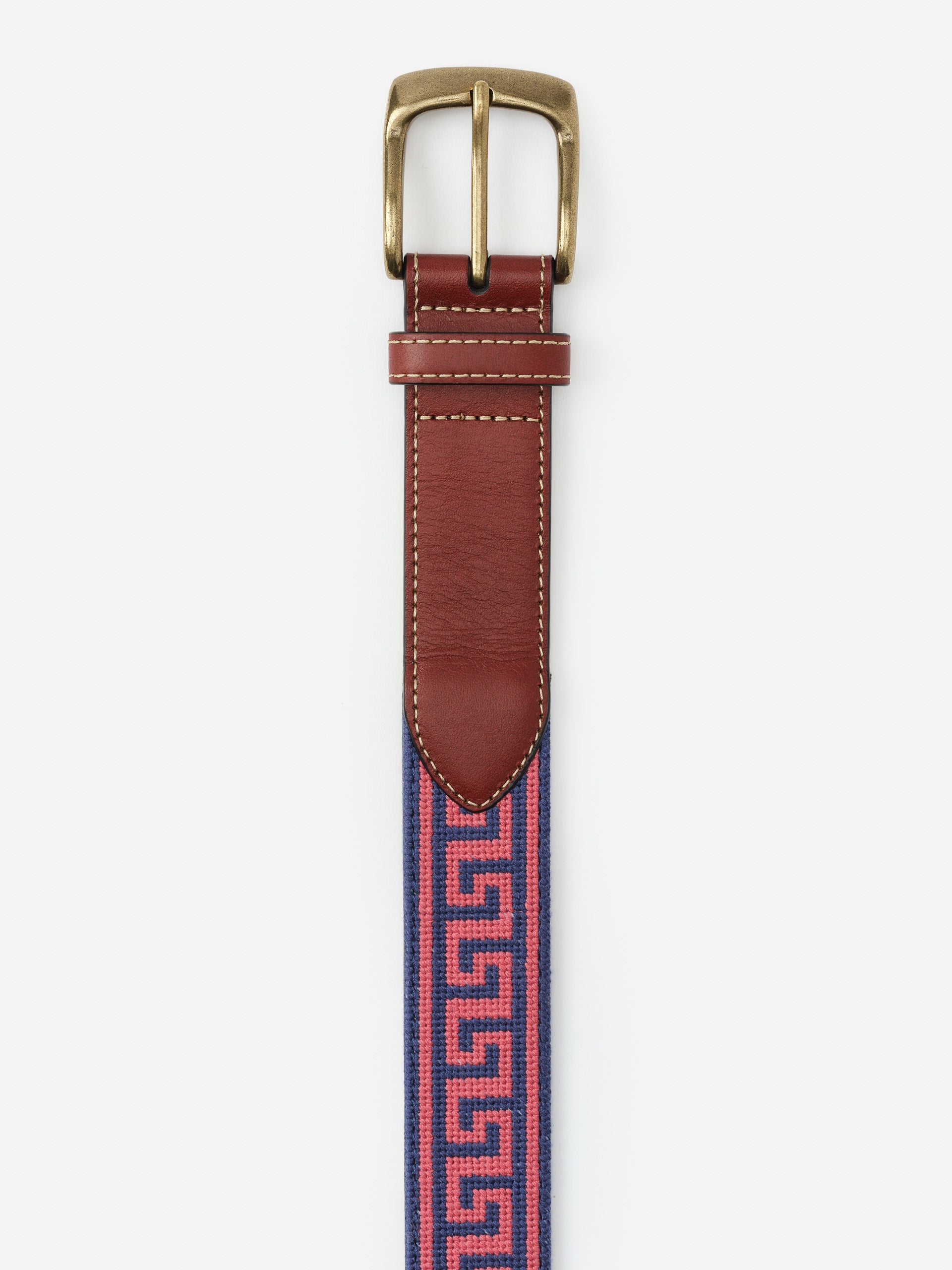 Close-up of the top half of a Needlepoint Belt in Greek Key by J.McLaughlin, featuring a brass buckle, rich brown leather trim, and a pink and navy needlepoint pattern with a Greek key design.