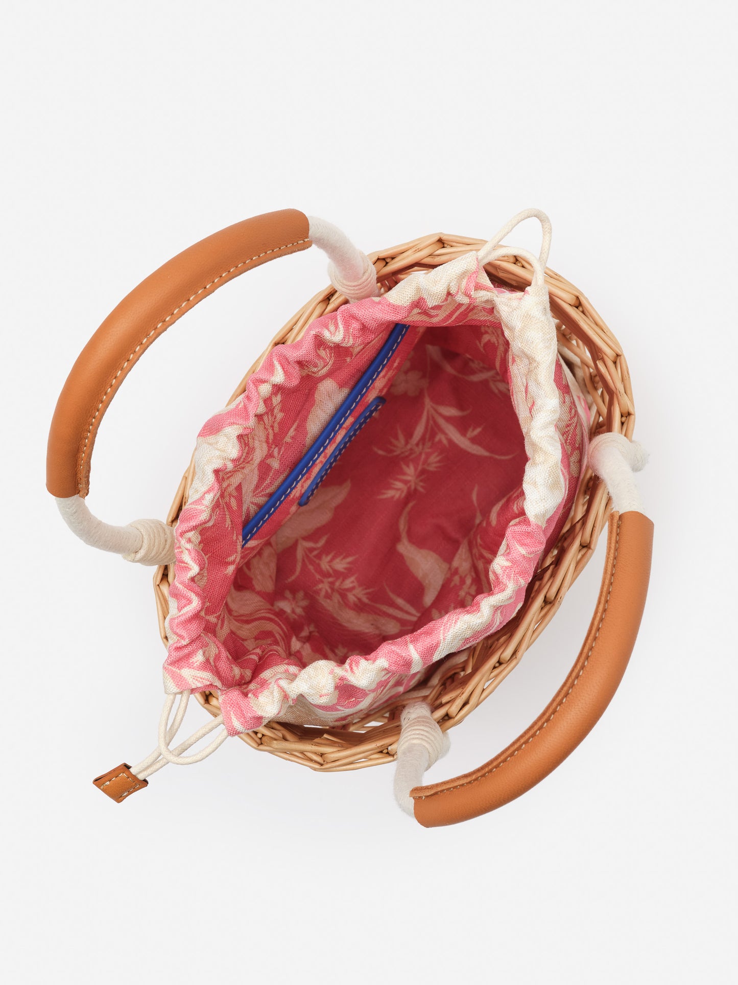 Top view of the Caryl Wicker Handbag in Giardino Toile by J.McLaughlin showing woven wicker body with leather handles and a pink patterned fabric interior drawstring closure, combining effortlessly stylish design with enduring craftsmanship for a legacy of timeless fashion. A destination for defining style. Life, Well-Lived.