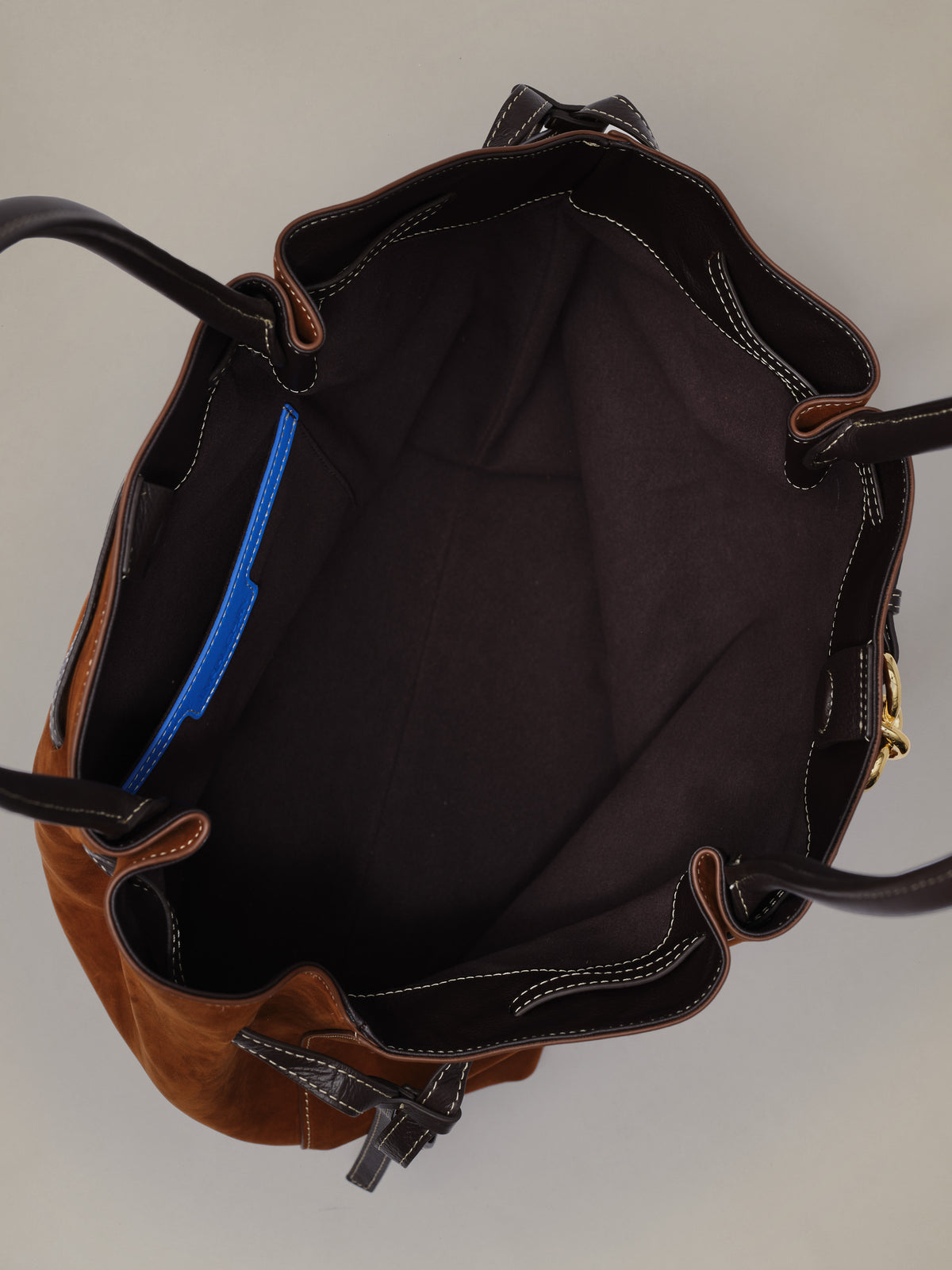 The Lex Suede Tote Bag by J.McLaughlin open to show its spacious dark lined interior blue zip pocket and sturdy handles