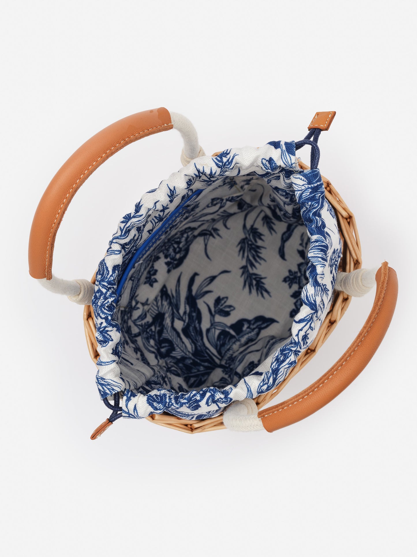 Top view of the Caryl Wicker Handbag in Giardino Toile by J.McLaughlin, showcasing its woven wicker body, leather handles, and blue floral fabric interior, embodying effortlessly stylish, enduring designs. A destination for defining style. Life, Well-Lived.