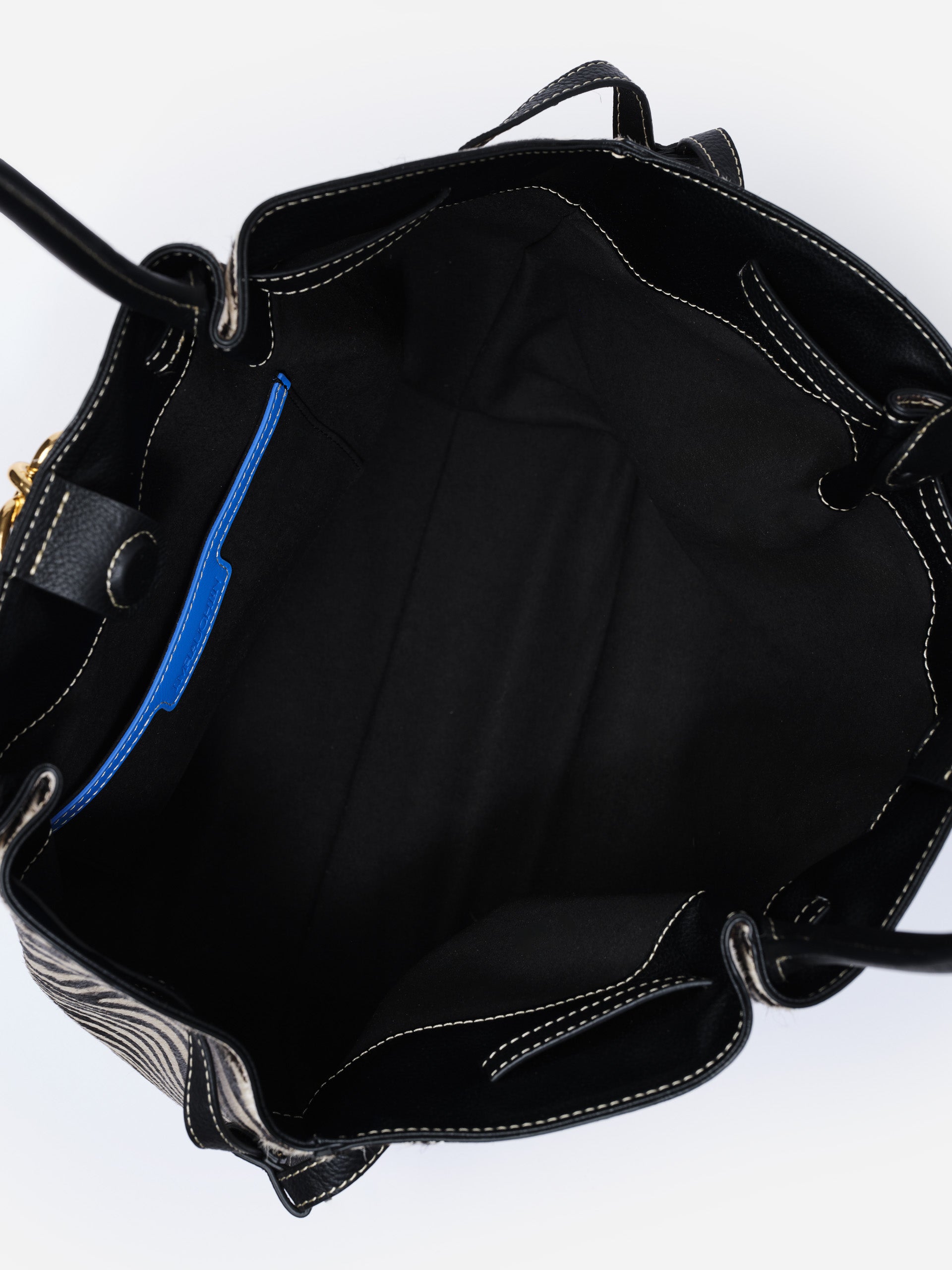Interior view of The Lex Pony Hair Tote Bag in Zebra Stripes by J. McLaughlin, showcasing spacious black lining with a blue accent pocket and detailed stitching.