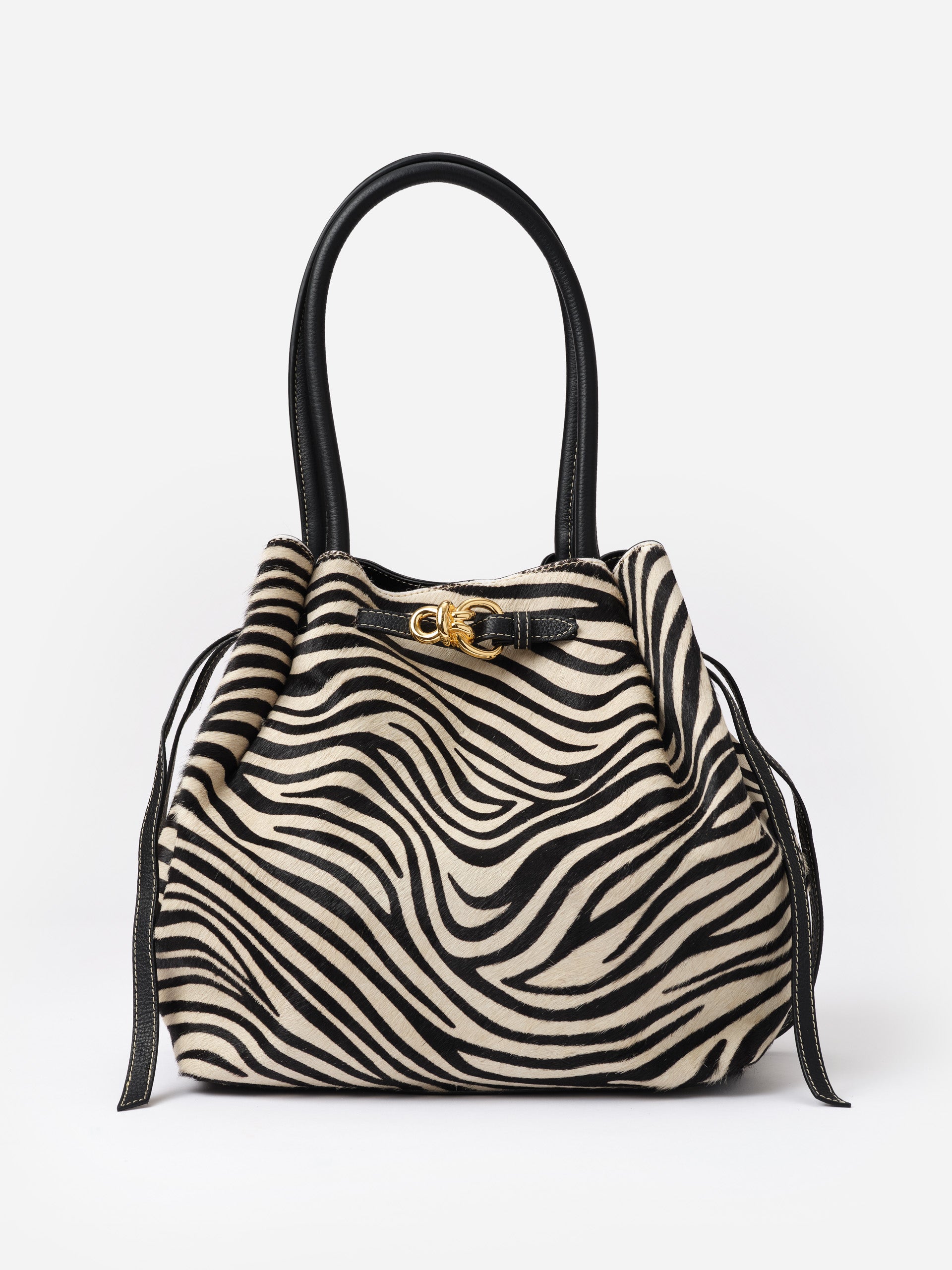 The Lex Pony Hair Tote Bag in Zebra Stripes by J.McLaughlin features a striking zebra pattern with black leather handles and gold hardware, blending timeless style with high-quality craftsmanship.
