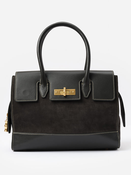 The Worth Leather Handbag by J.McLaughlin, a structured black bag with polished gold-tone bamboo-inspired turnlock, showcasing timeless design and impeccable craftsmanship.