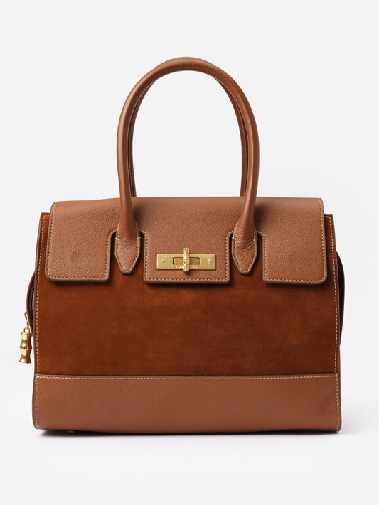 The Worth Leather Handbag by J.McLaughlin features a structured brown leather design with dual handles and a polished gold-tone bamboo-inspired turnlock closure, combining timeless style and craftsmanship.