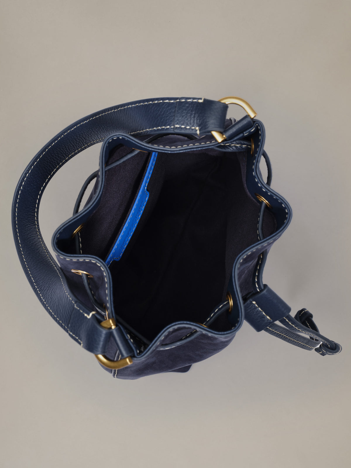 The Newbury Suede Bucket Bag by J.McLaughlin in navy suede with an open bucket silhouette gold hardware and drawstring closure