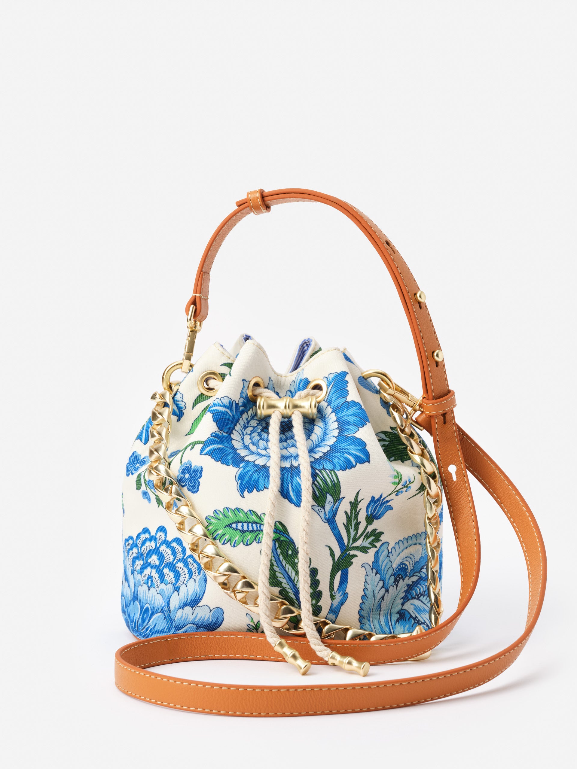 Daisy Bucket Bag in Mini Cerulean Garden by J.McLaughlin features a floral print in blue and green with tan leather straps, showcasing effortlessly stylish, enduring designs and a legacy of timeless fashion.