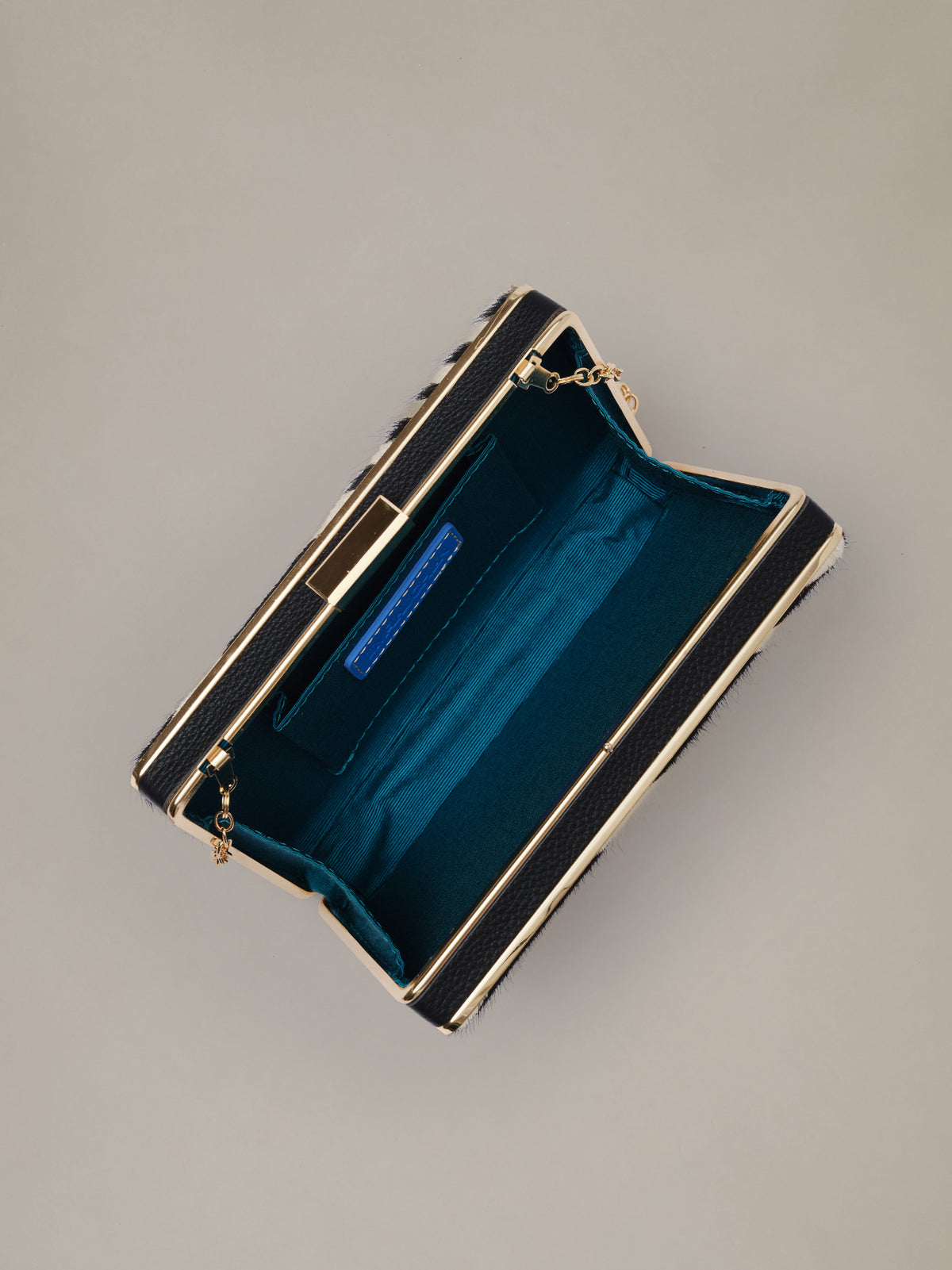 The Palm Pony Hair Clutch in Zebra Stripes by J.McLaughlin shown open with a teal lined interior and gold chain detail