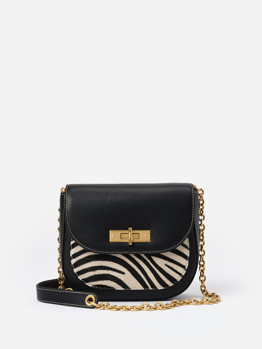 Waverly Leather Handbag in Zebra Stripes by J.McLaughlin featuring a compact black leather design with zebra print accent and a gold chain strap, blending timeless style and practicality.