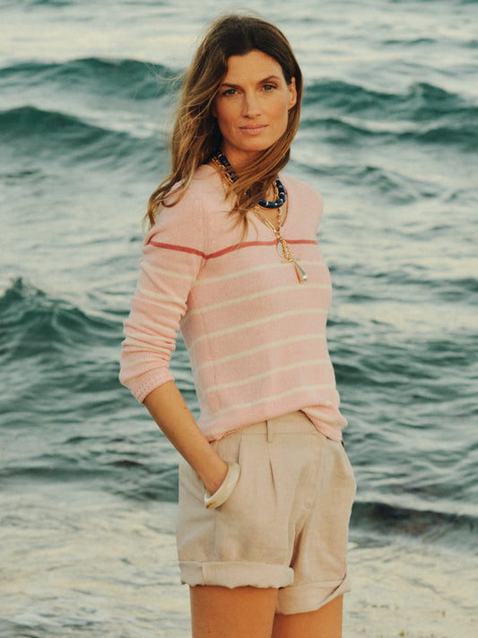 Woman wearing a Ramona Linen Blend Sweater in Stripe by J.McLaughlin, styled with rolled beige shorts and statement necklaces at the seaside, showcasing effortlessly stylish, enduring designs with innovative fabrics. A destination for defining style. Life, Well-Lived.