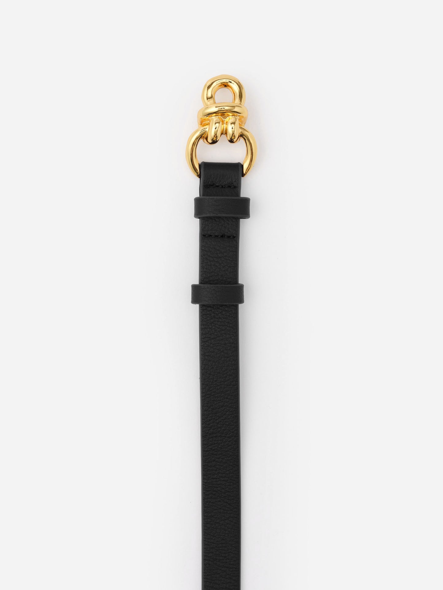 Close-up of the black Natalie Leather Belt by J.McLaughlin featuring a slim profile and distinctive gold knot hardware, embodying effortlessly stylish and enduring design.